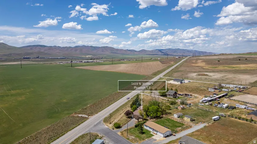 Expansive property featuring a paved road frontage, surrounding green fields, and distant mountain ranges