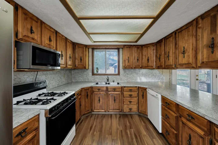 U-shaped kitchen featuring wood cabinetry, stone-look countertops, a built-in microwave, and wood-finish flooring