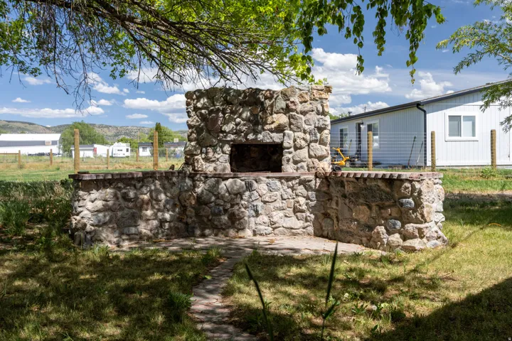 Stone outdoor fireplace with a built-in cooking area, integrated stone counters, and a flagstone patio base