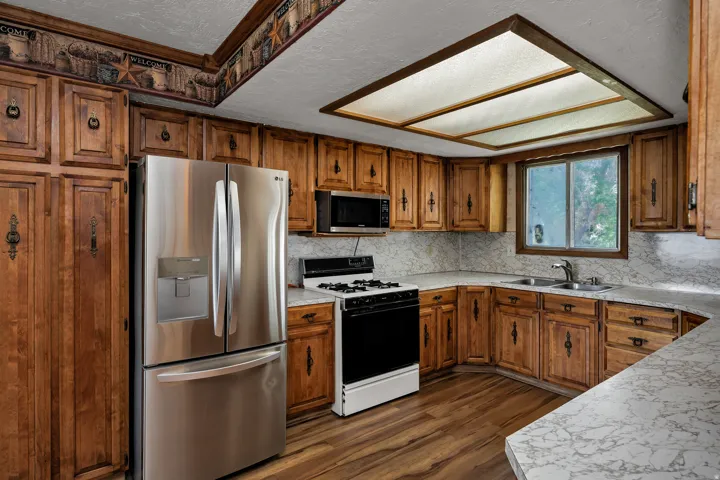 Kitchen featuring wood-finish cabinetry with decorative hardware, stainless steel refrigerator, built-in microwave, gas range, and wood-finish flooring