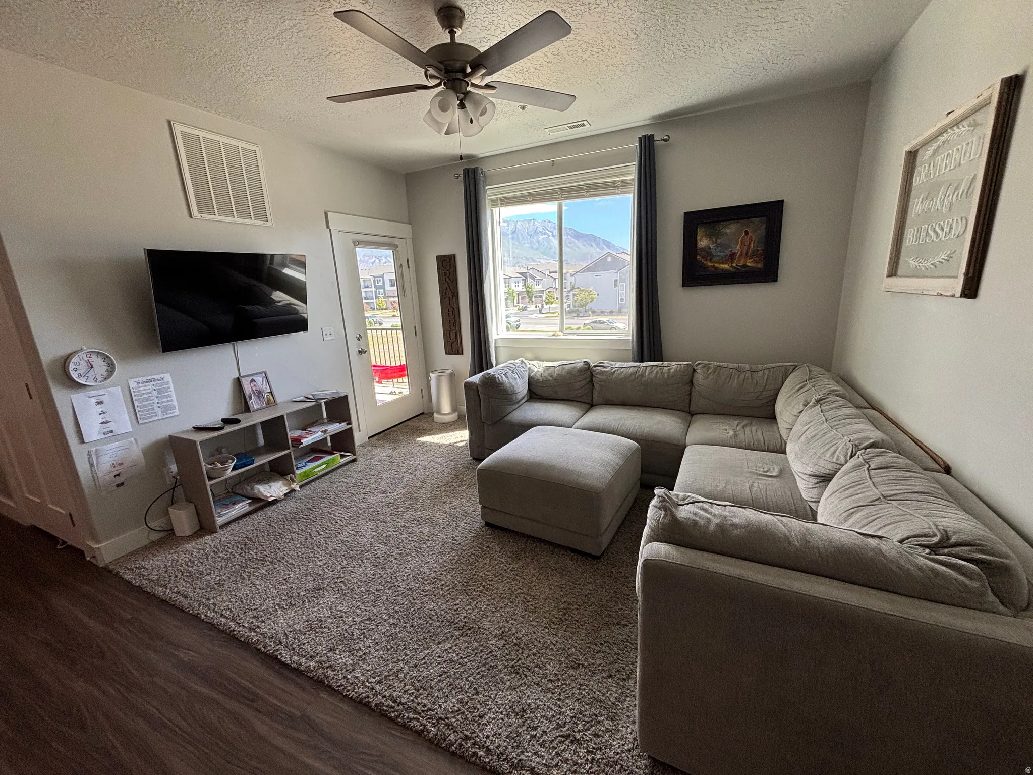 Spacious living area featuring a ceiling fan with integrated lighting, wood-finish flooring, and light-colored walls