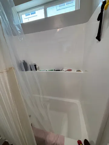 White shower surround featuring an integrated soap shelf and a window above