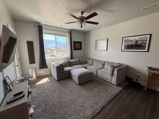 Living area featuring a ceiling fan with integrated lighting, a large window, and wood-finish flooring