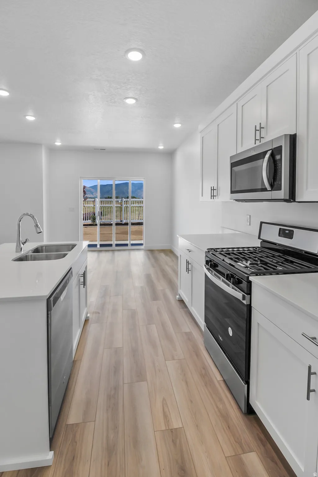 Modern kitchen featuring white shaker cabinetry, stainless steel appliances, light wood-finish flooring, and white countertops