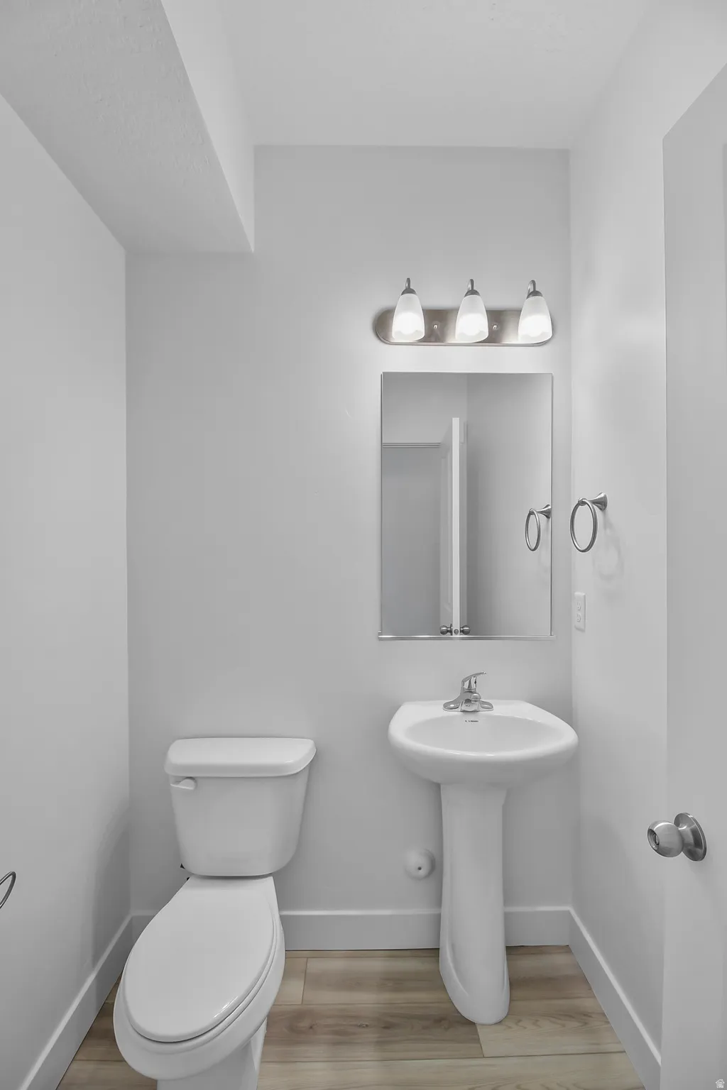 Bathroom featuring a pedestal sink, wall-mounted mirror, and a three-light vanity fixture