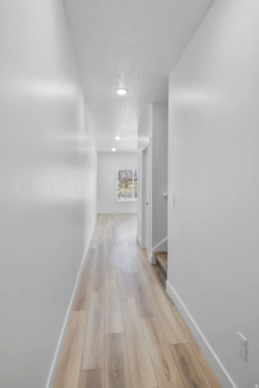 Hallway featuring recessed lighting, light wood-finish flooring, white baseboards, and a neutral wall palette
