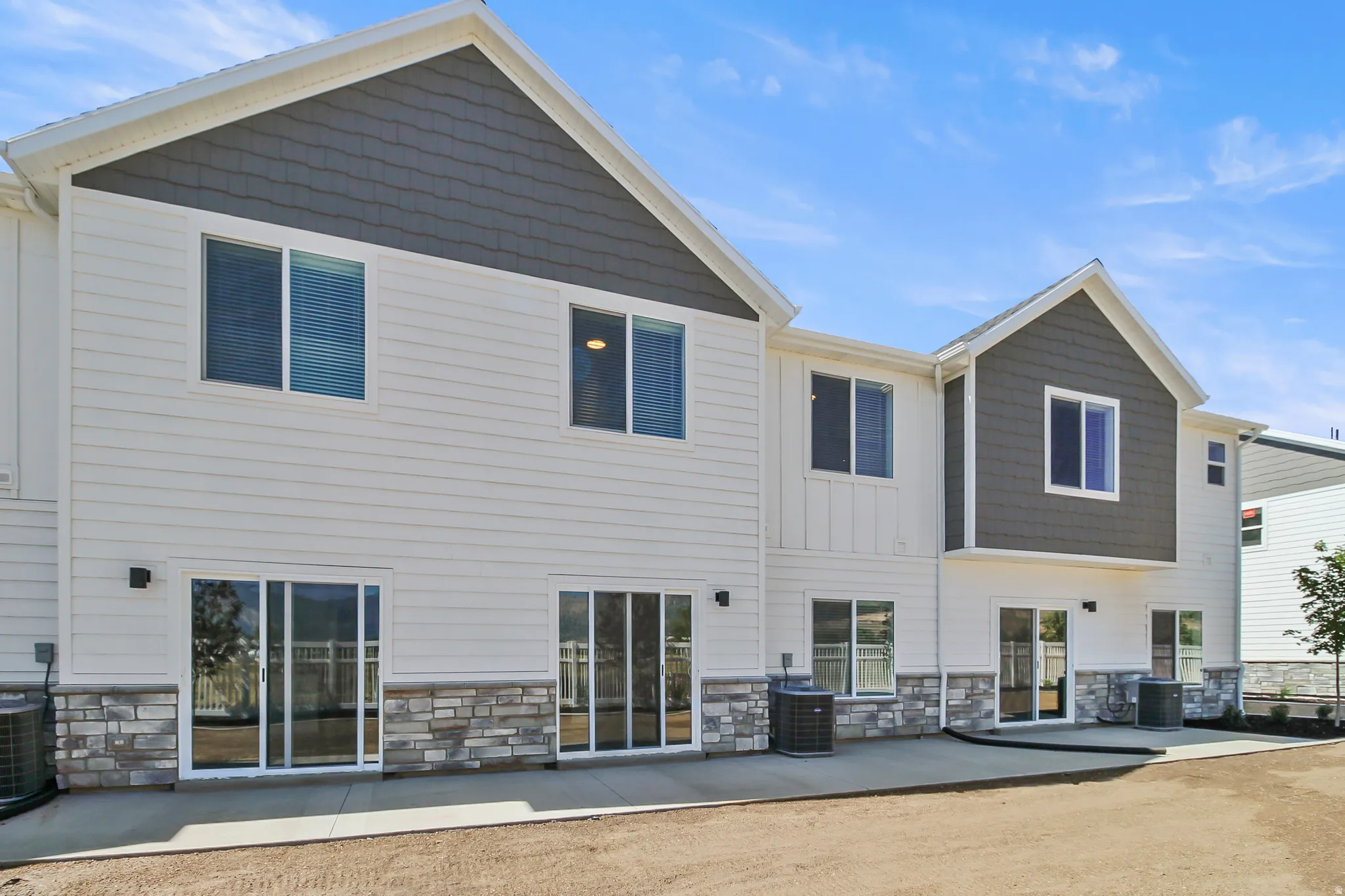 Contemporary multi-level exterior featuring white horizontal siding, dark gray shake siding accents, and a stone veneer foundation