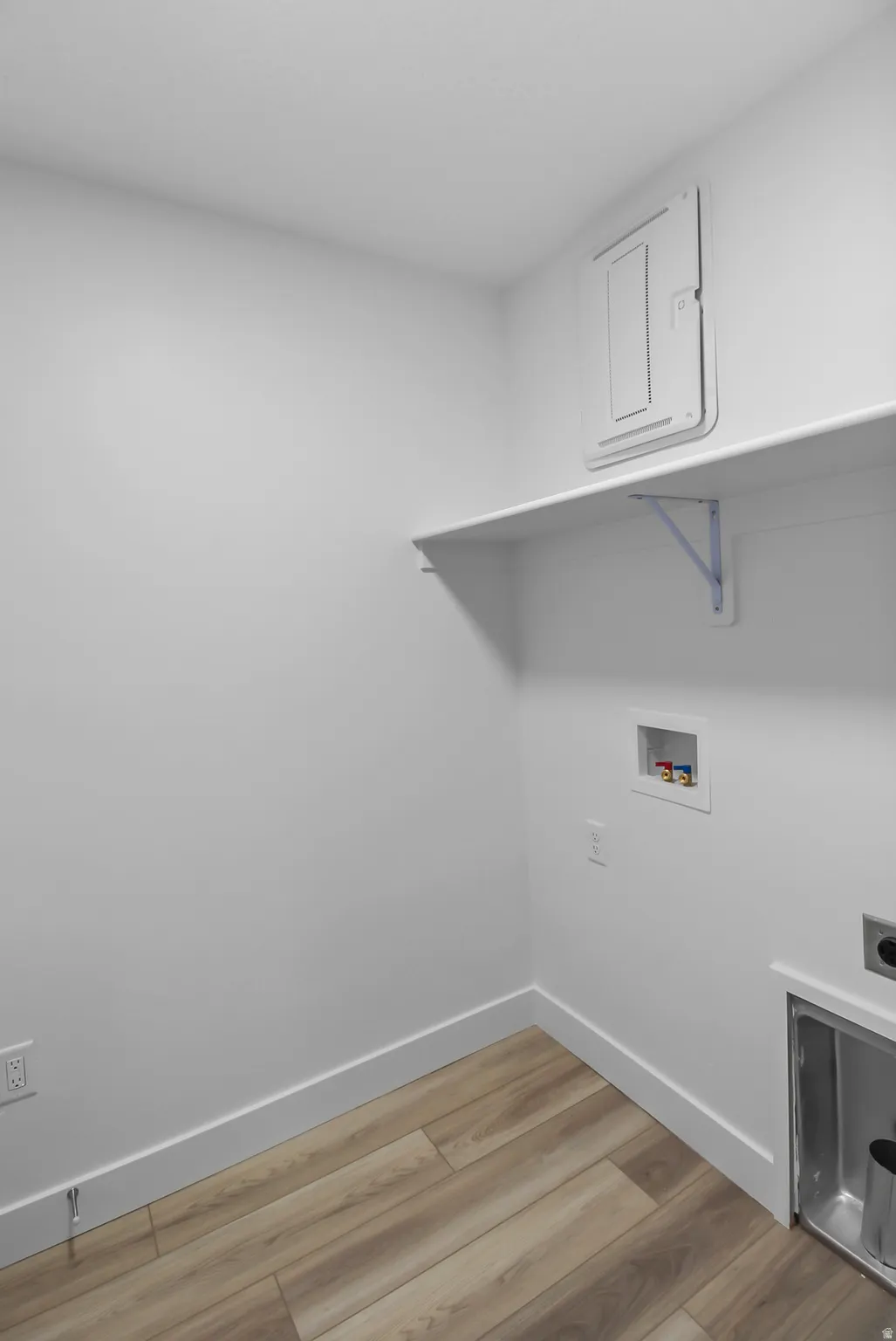 Dedicated laundry space featuring wood-finish flooring, white baseboards, a built-in wall shelf with brackets, and appliance hookups