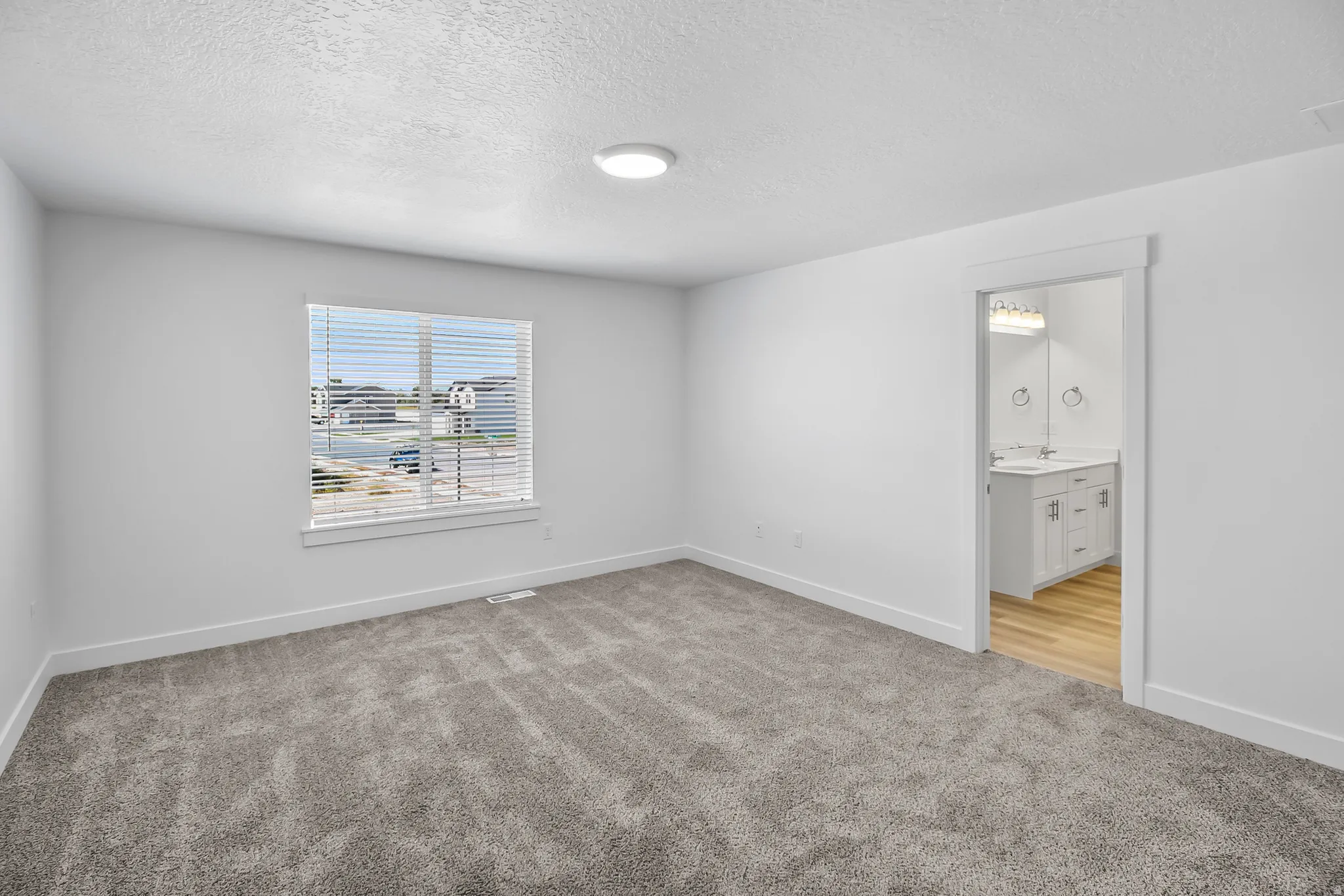 Spacious room featuring neutral carpeting, white walls, and a single window with blinds