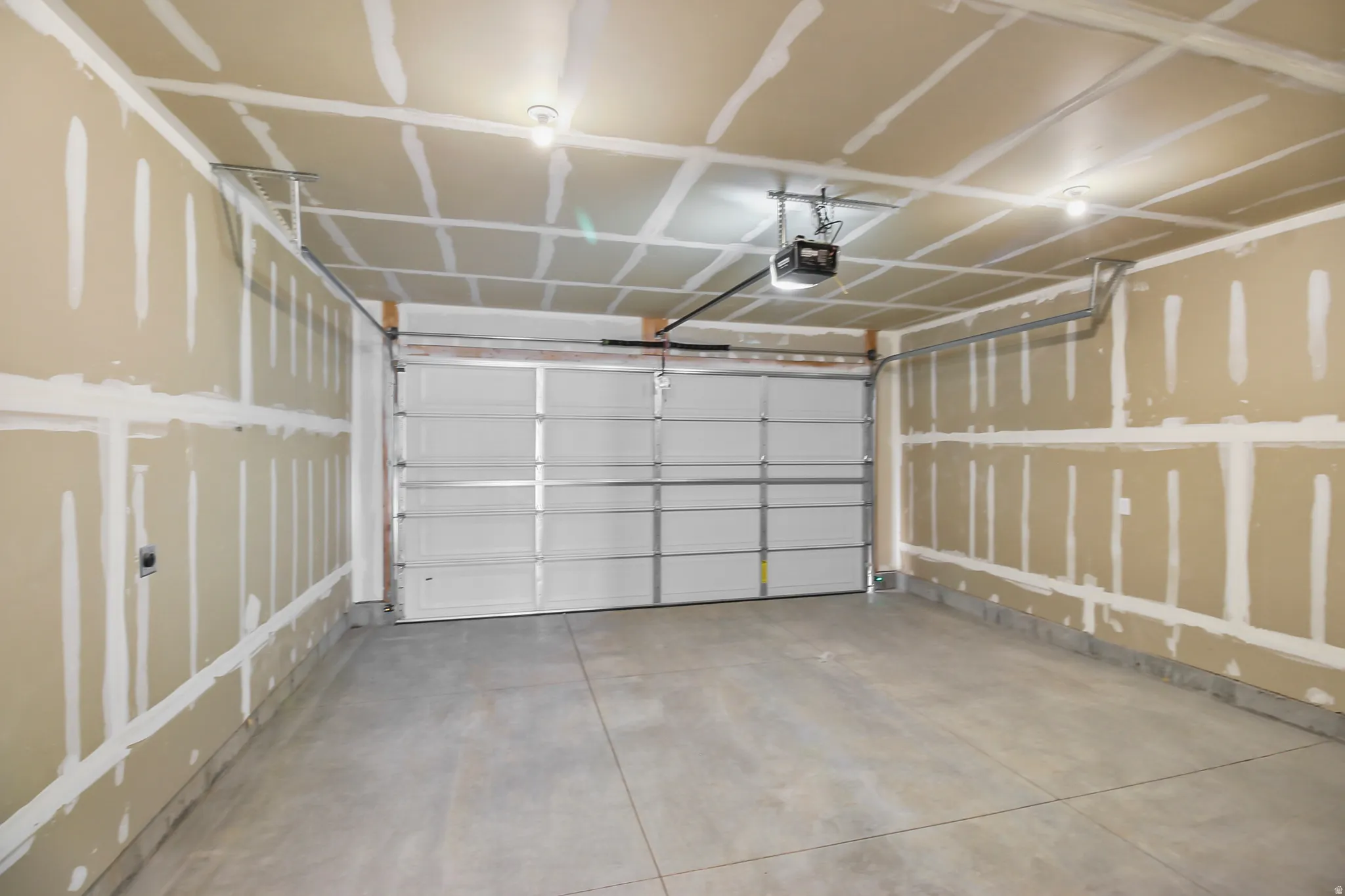 Spacious garage featuring a concrete floor, an overhead door with an automatic opener, and installed lighting fixtures