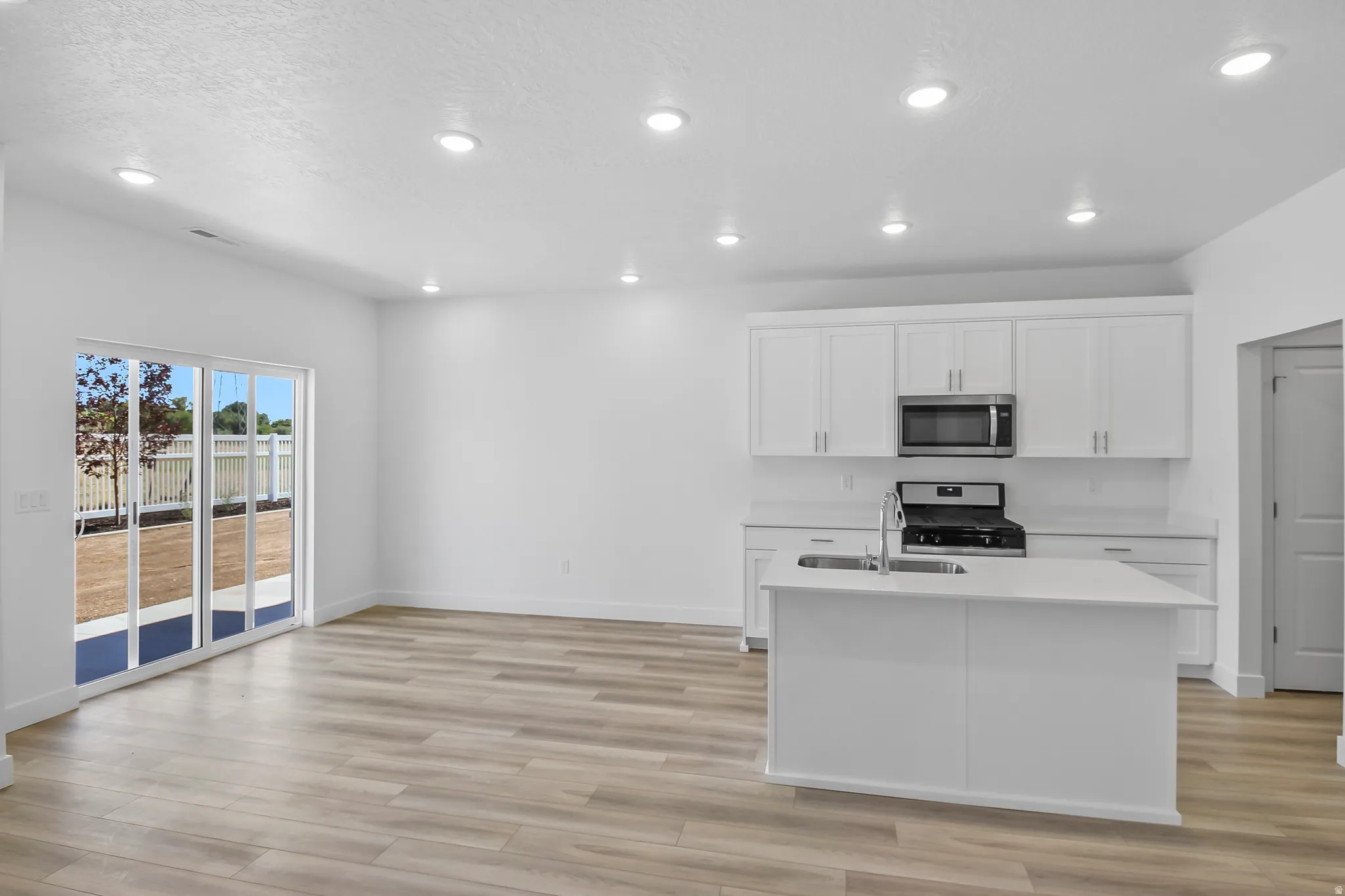 Modern kitchen featuring white cabinetry, a central island with an undermount sink, stainless steel appliances, and recessed lighting