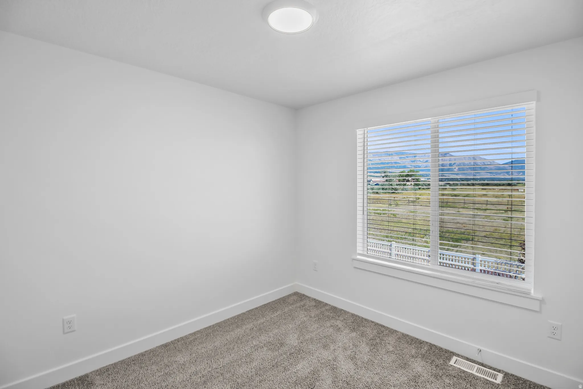 Room with a large window featuring horizontal blinds, offering a mountain backdrop and expansive scenery