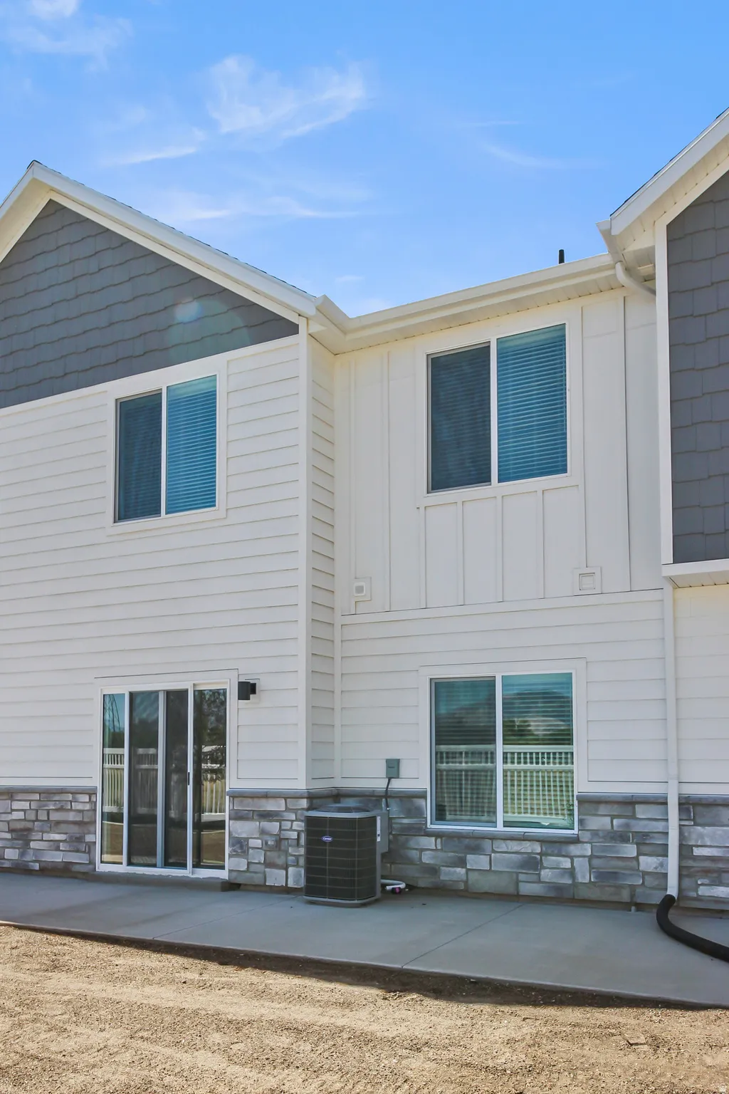 Rear exterior featuring horizontal and board and batten siding, stone veneer accents, and a sliding glass door