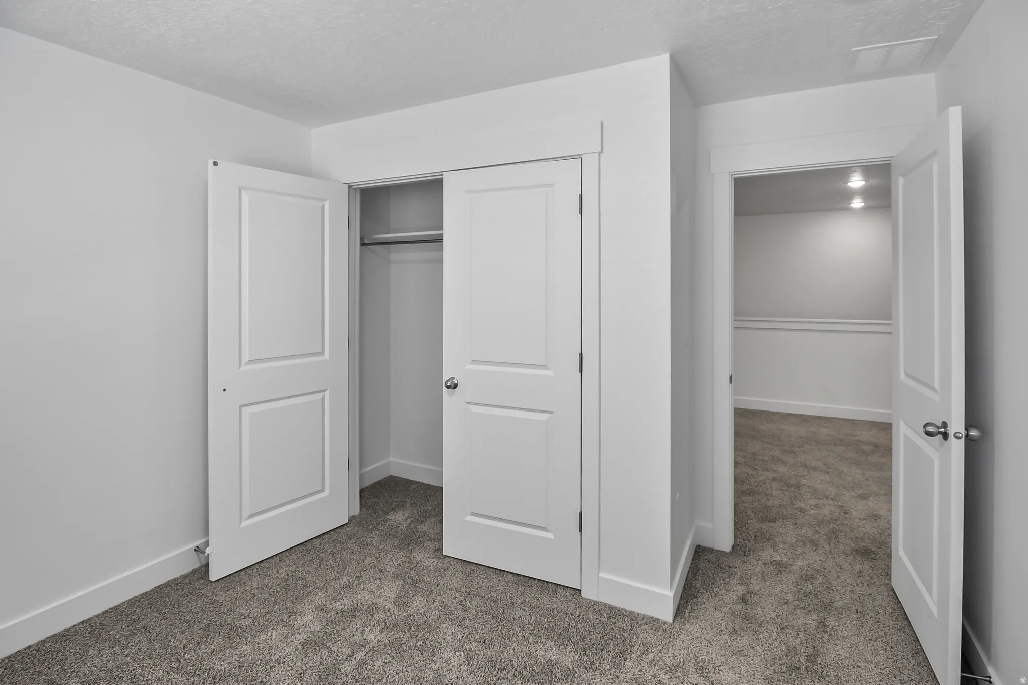 Interior space featuring light gray walls, gray carpet flooring, white trim, and a bi-fold closet with a hanging rod