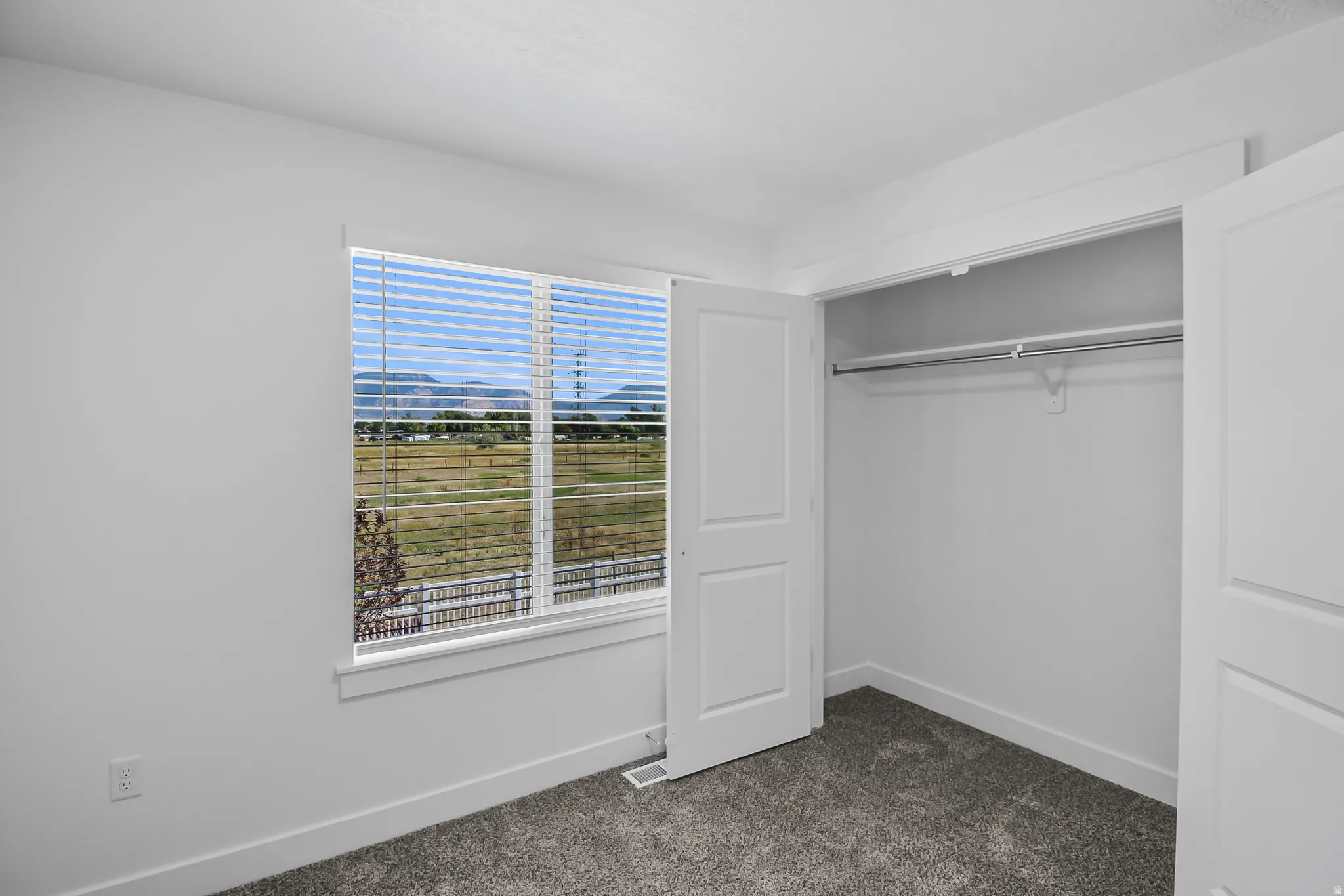 Bedroom featuring a large window with horizontal blinds, a neutral color palette, plush carpet flooring, and a double-door closet with a hanging rod
