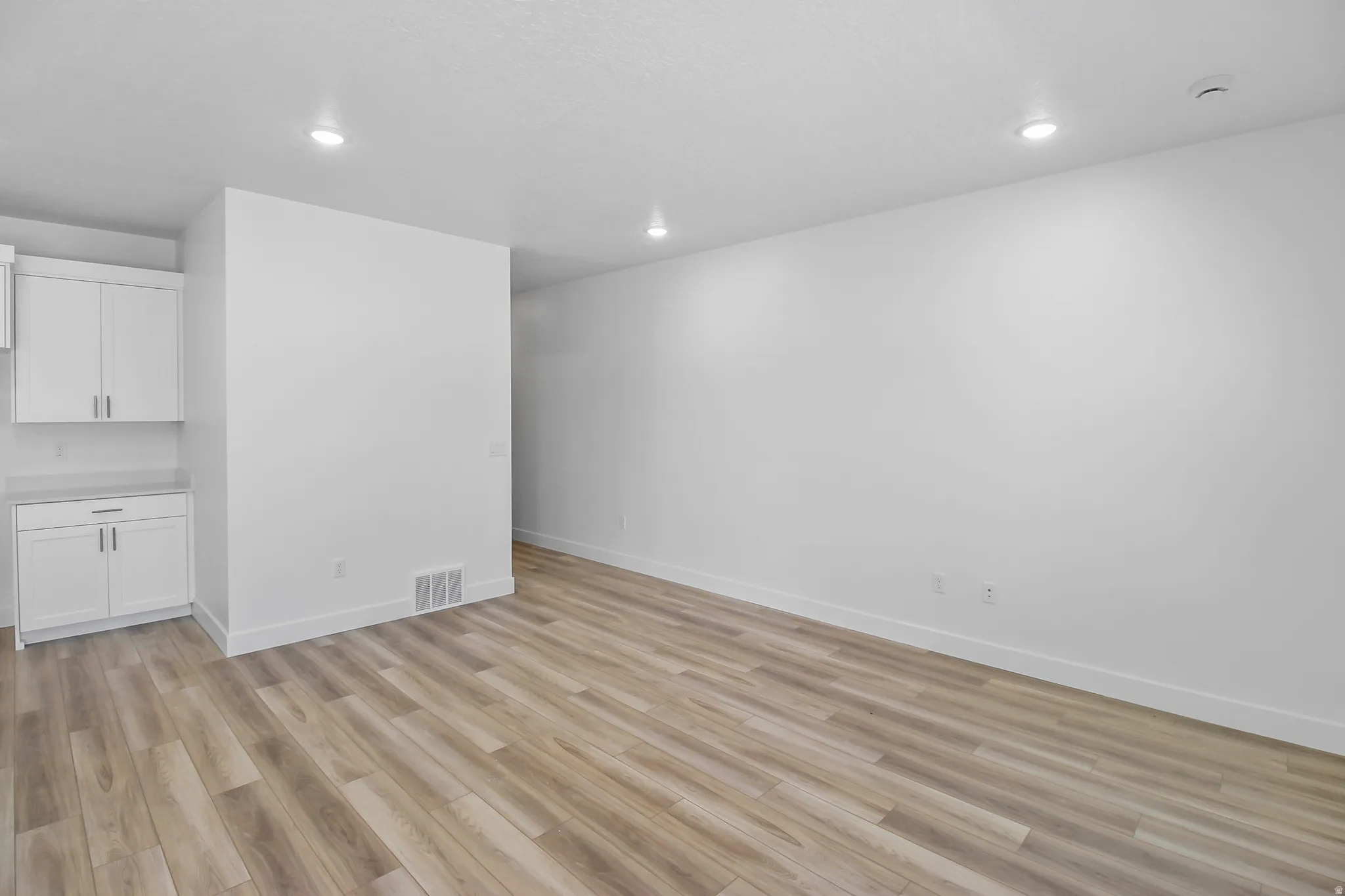 Expansive room featuring light wood-finish flooring, recessed lighting, and white baseboards