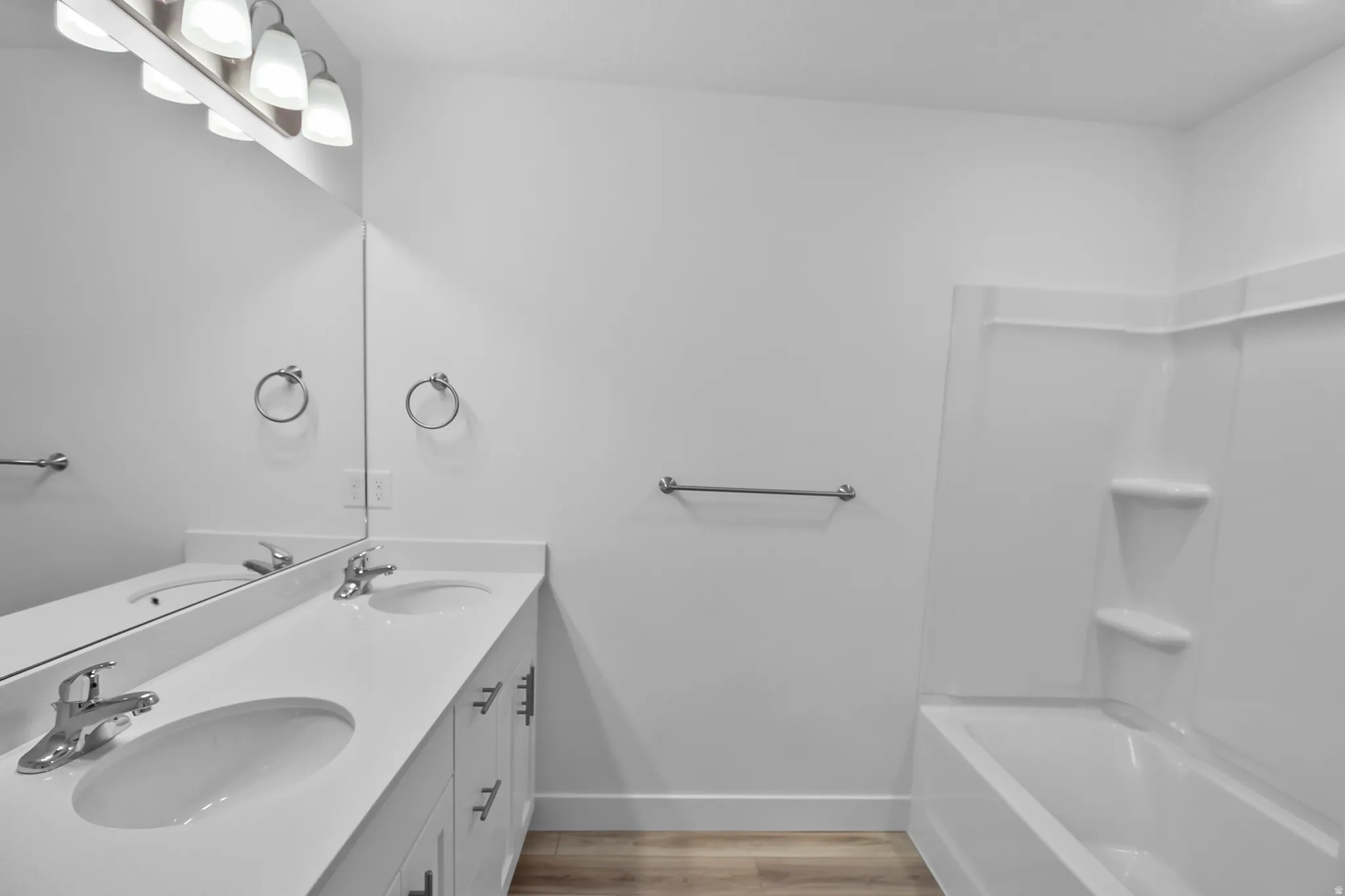 Bathroom featuring a double vanity with integrated sinks, white cabinetry with silver hardware, an overhead light fixture, and a white tub and shower combination