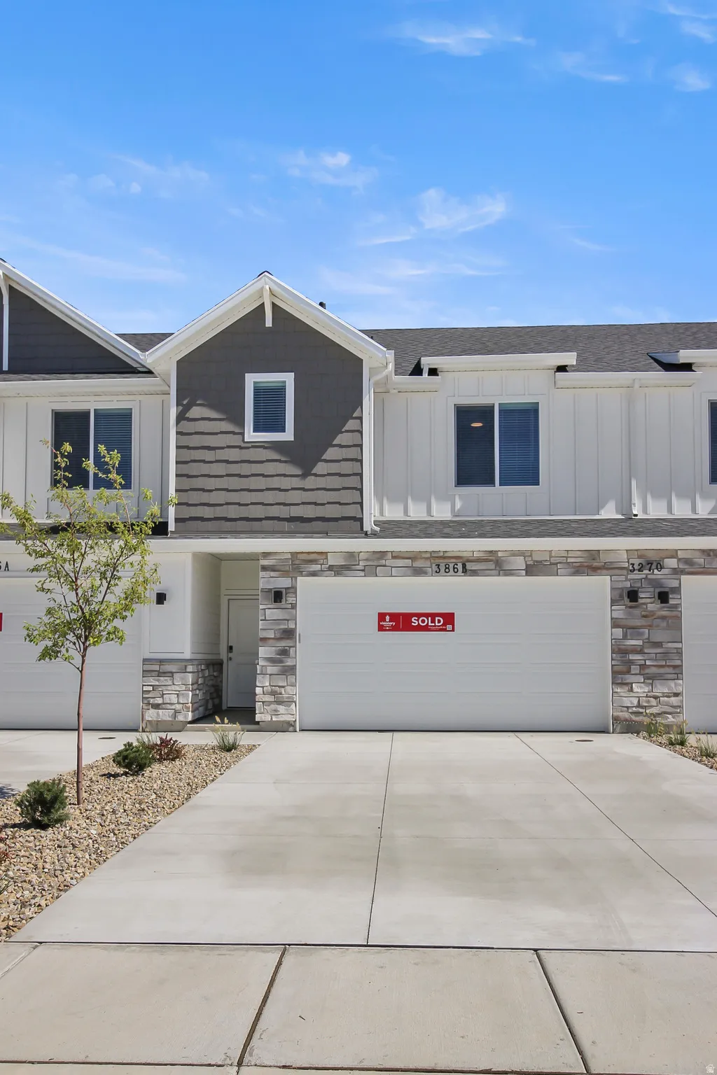 Modern townhome exterior featuring white vertical siding, dark gray horizontal shingles, and stone veneer accents