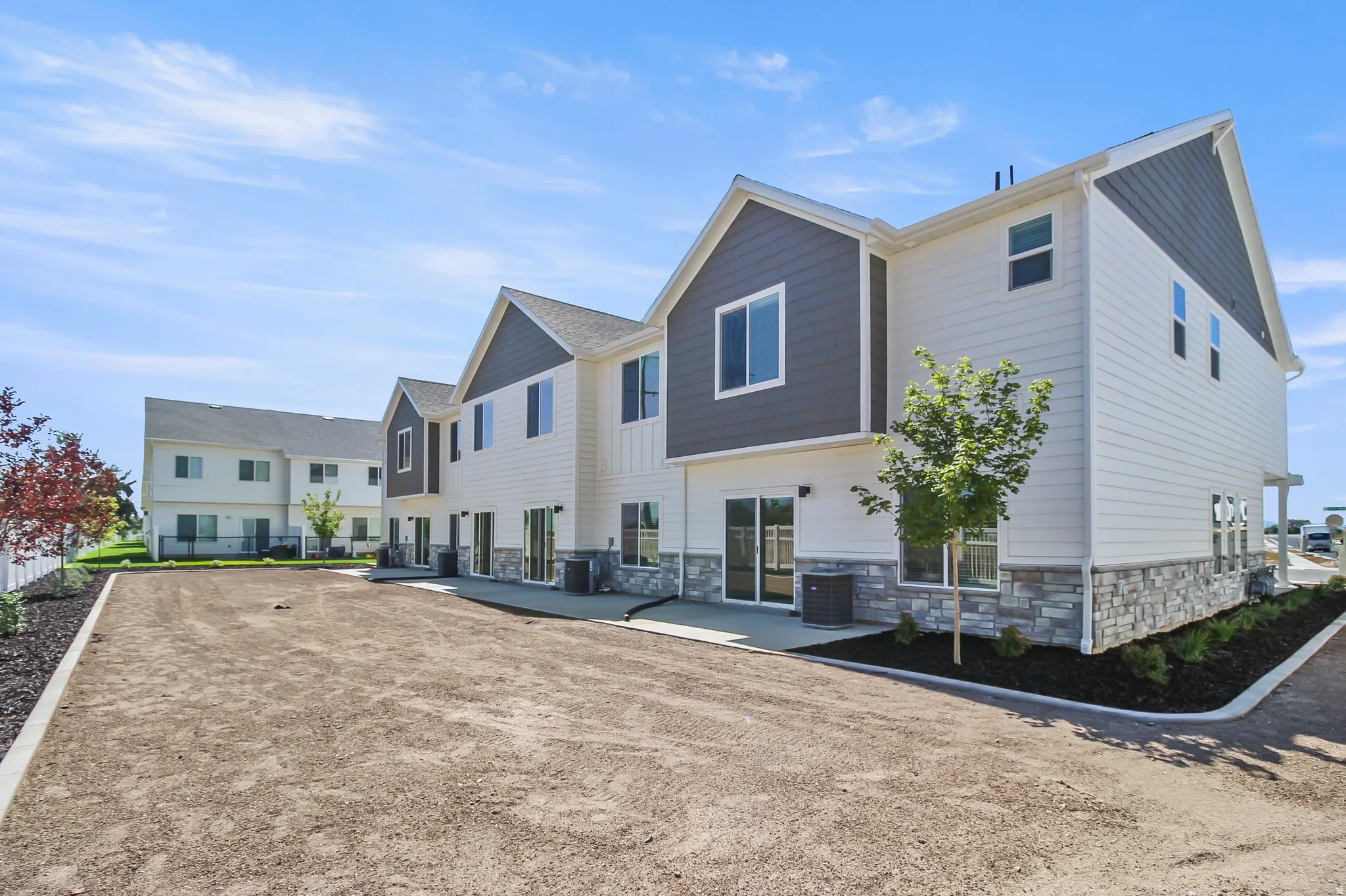 Contemporary townhome architecture featuring white siding, grey gables, stone accents, and multiple sliding glass doors opening to a rear patio