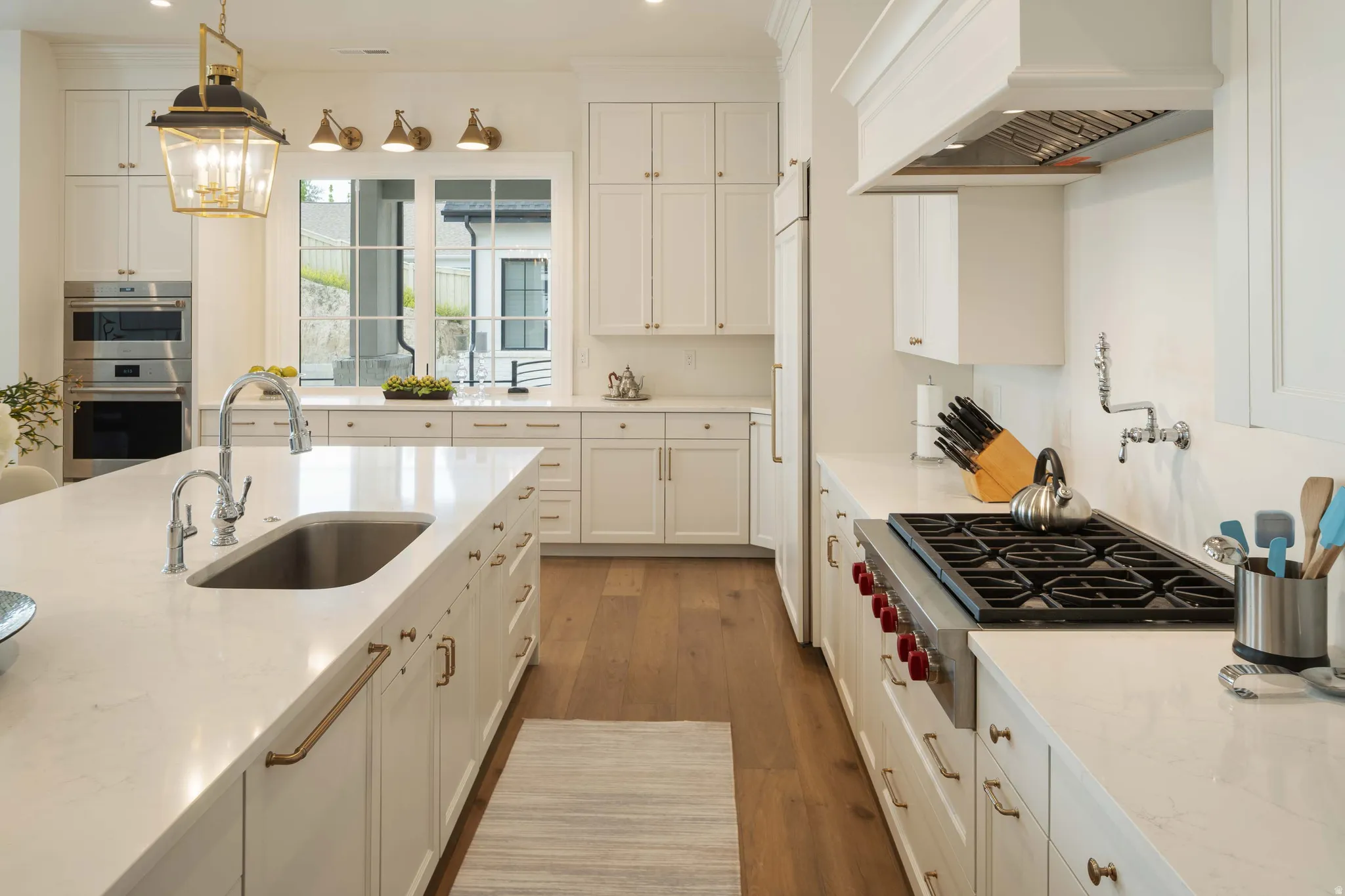 Gourmet kitchen featuring a large island with an undermount sink, built-in double oven, gas range with pot filler, extensive cabinetry, and wood-finish flooring