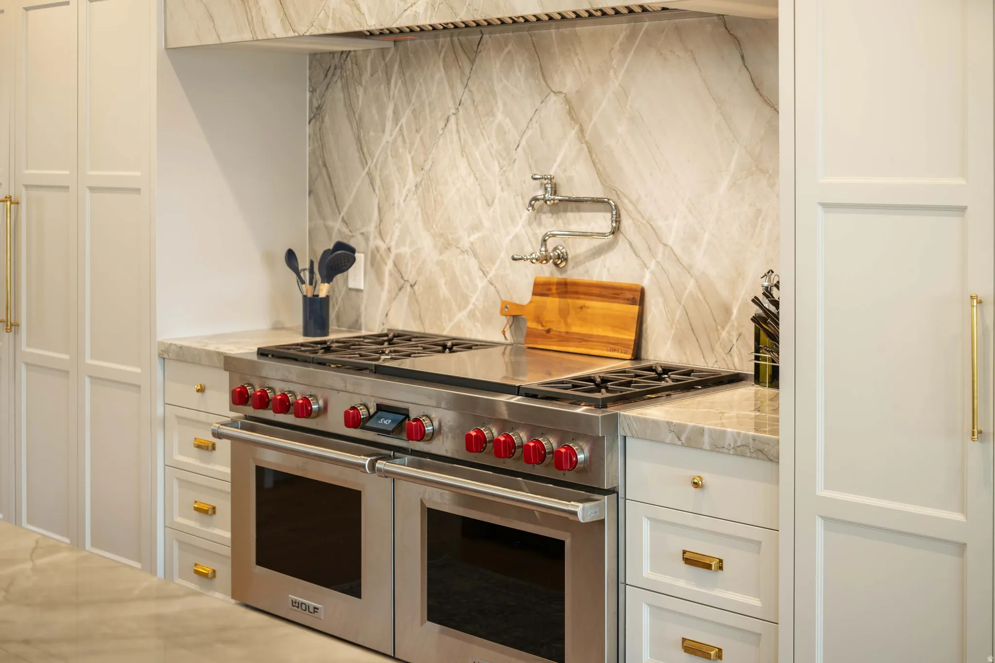 Stainless steel range with red knob accents, featuring a matching range hood and a marble-patterned backsplash