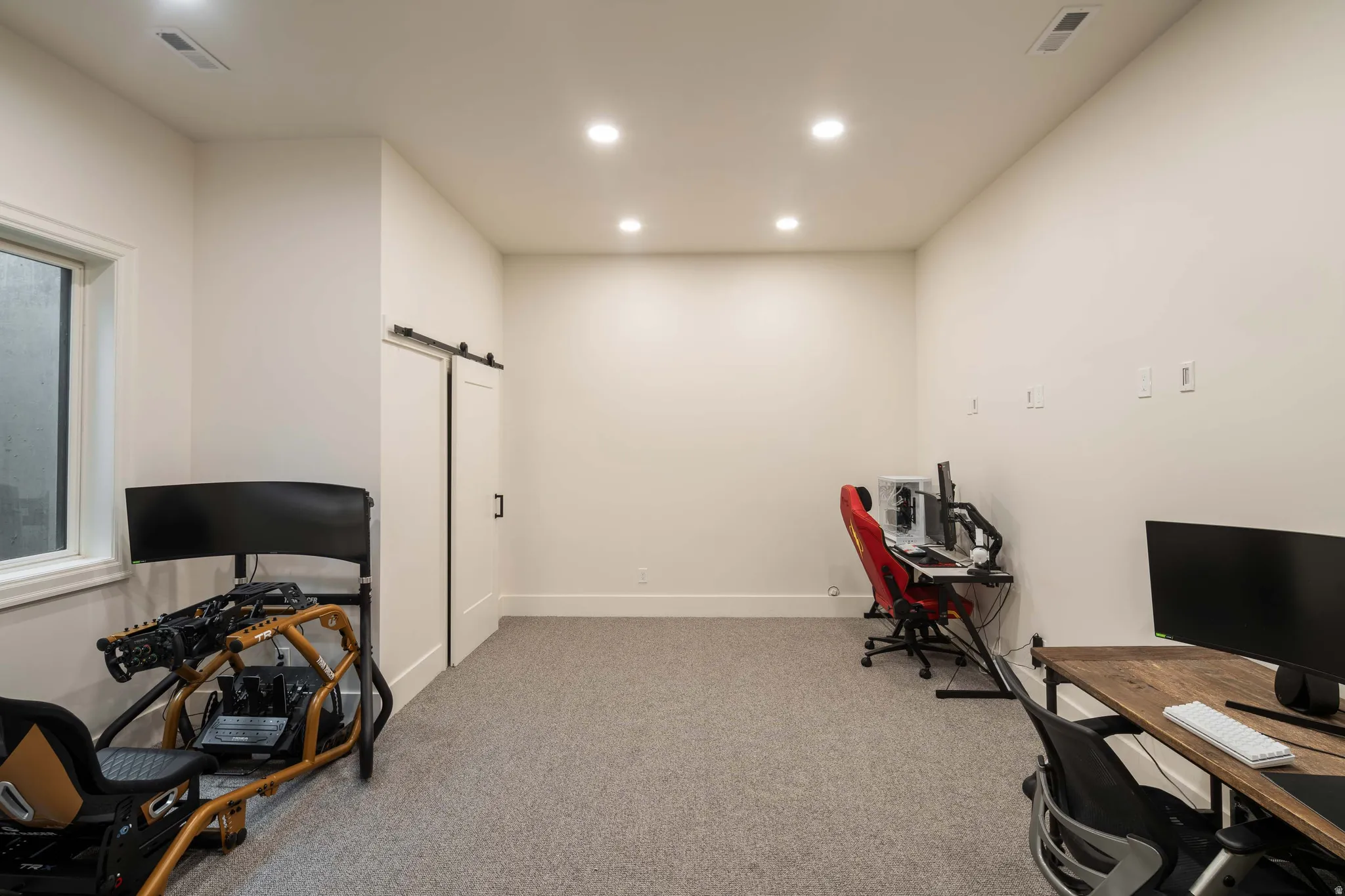 Spacious room featuring neutral wall paint, recessed lighting, gray carpet flooring, a barn door, and a white-framed window