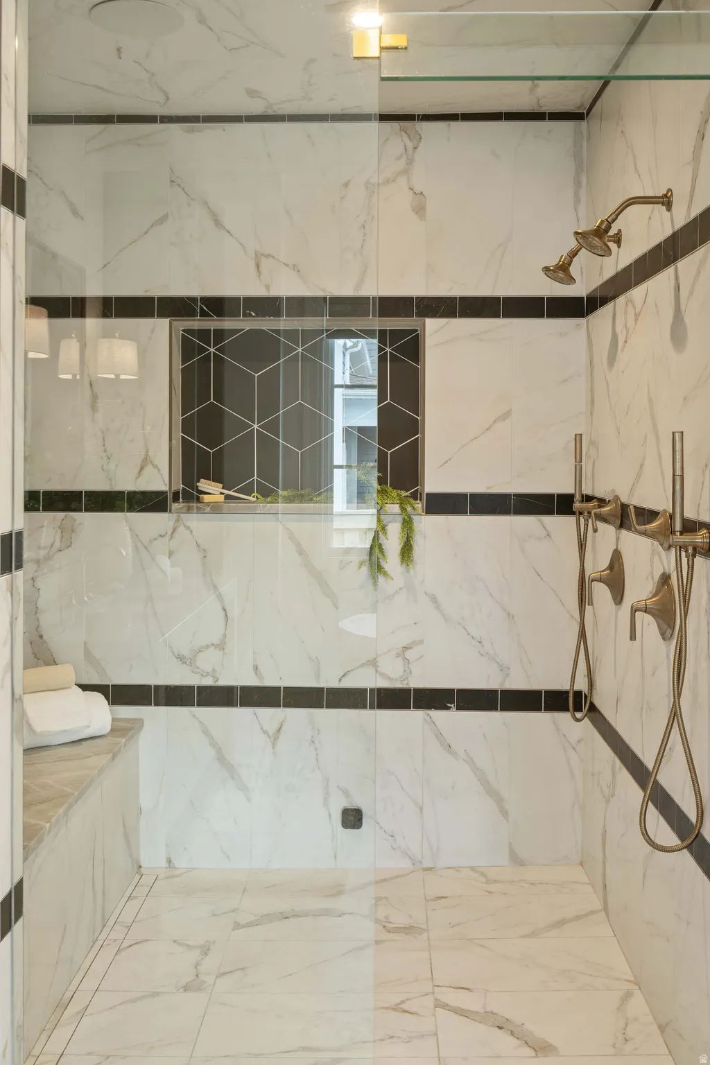 Shower with full-height white veined tile, black accent banding, and a built-in bench