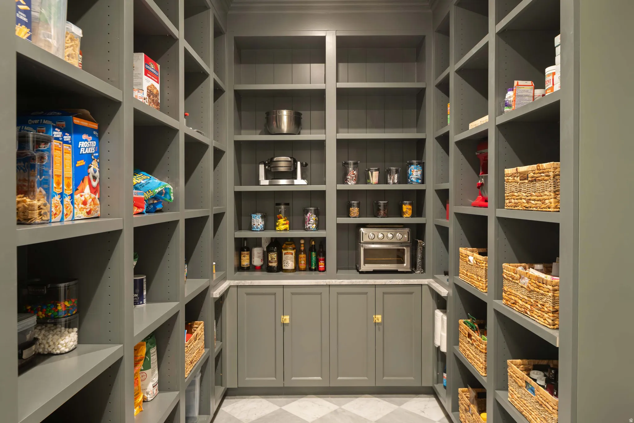 Custom pantry featuring extensive built-in shelving, integrated lower cabinetry, a light-toned countertop, and patterned floor tiling