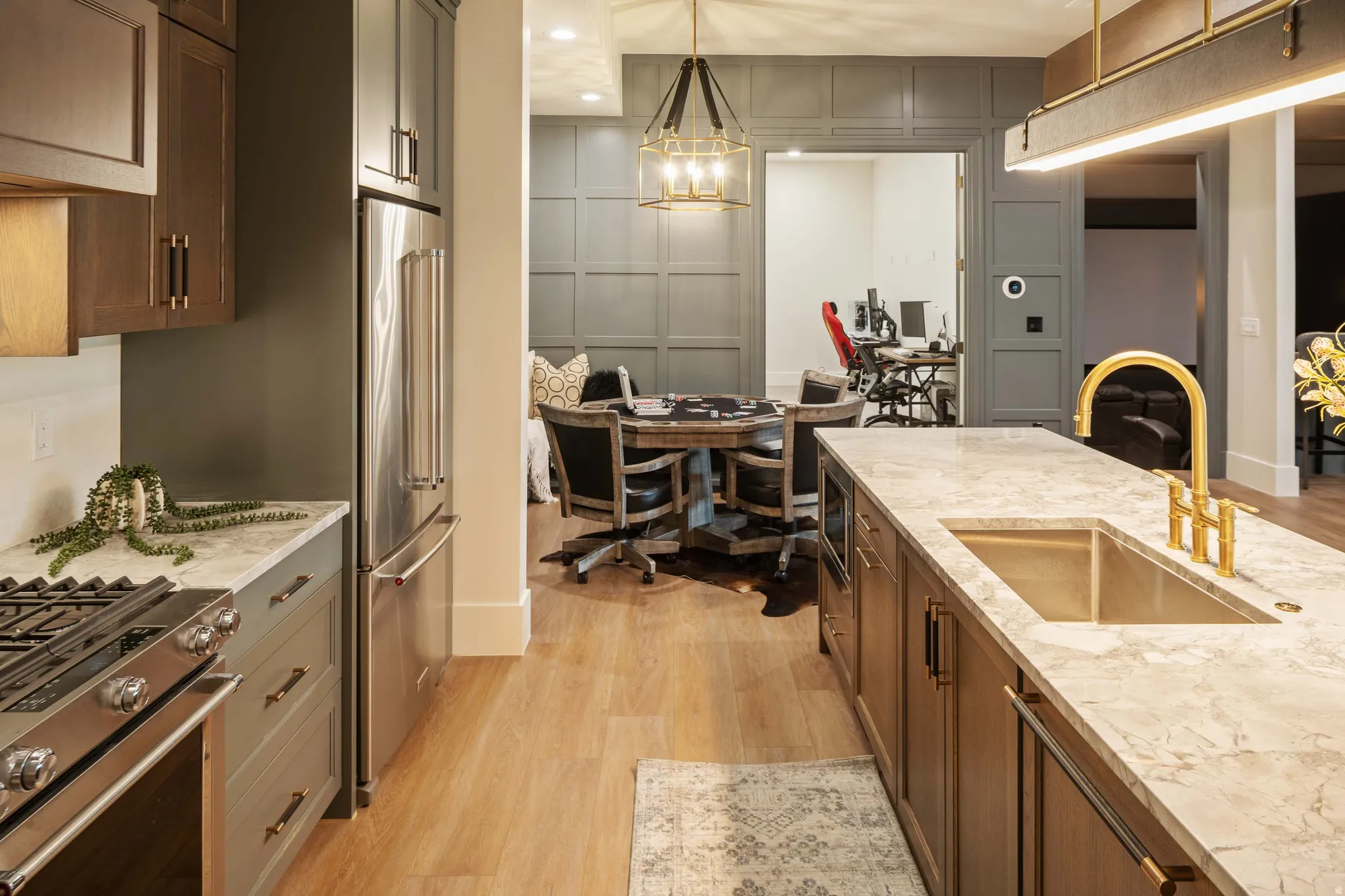 Gourmet kitchen featuring a gas range, stainless steel appliances, stone countertops, and a large center island with an undermount sink and brass faucet