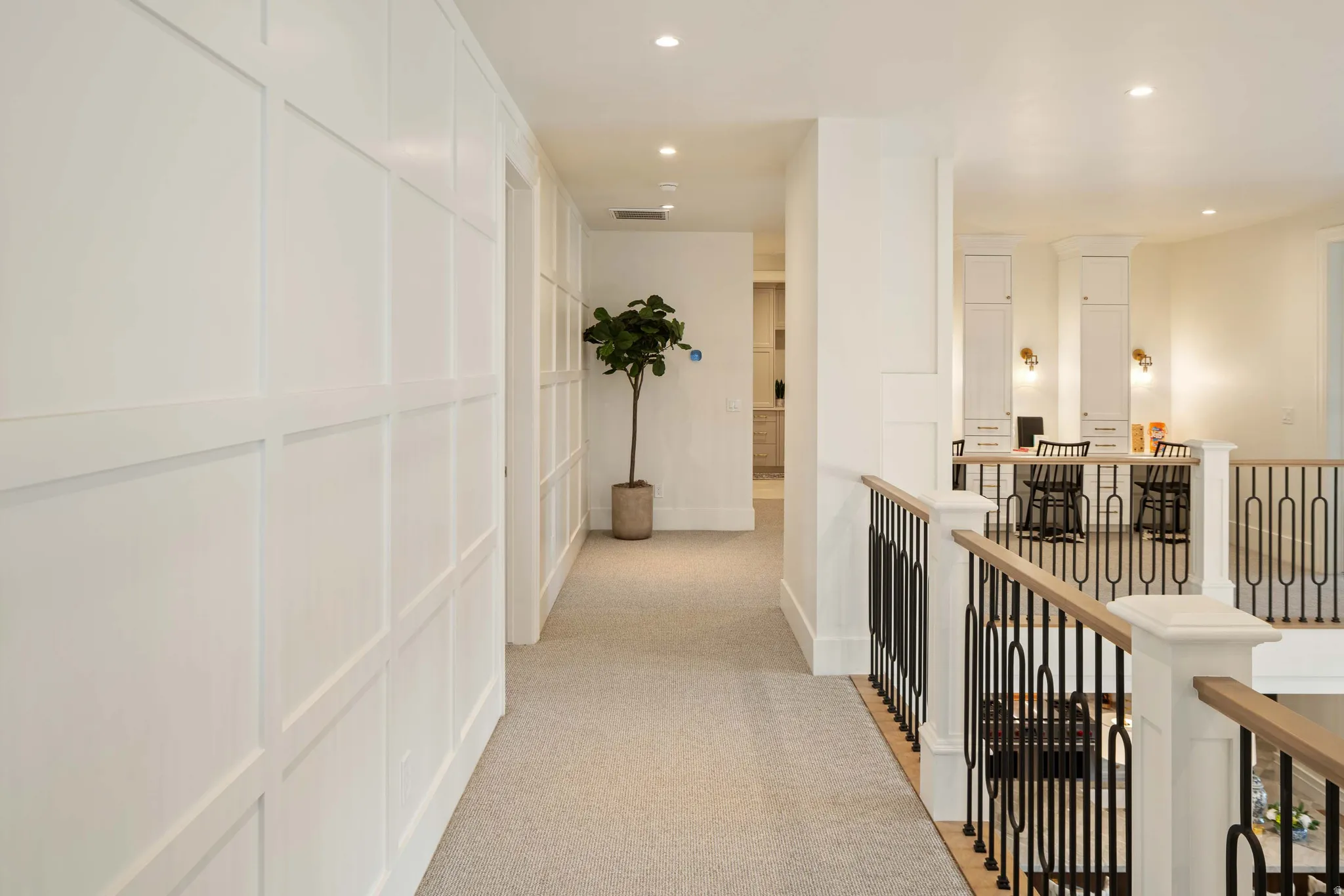White paneled wall detailing a hallway with recessed lighting and light-toned carpeting