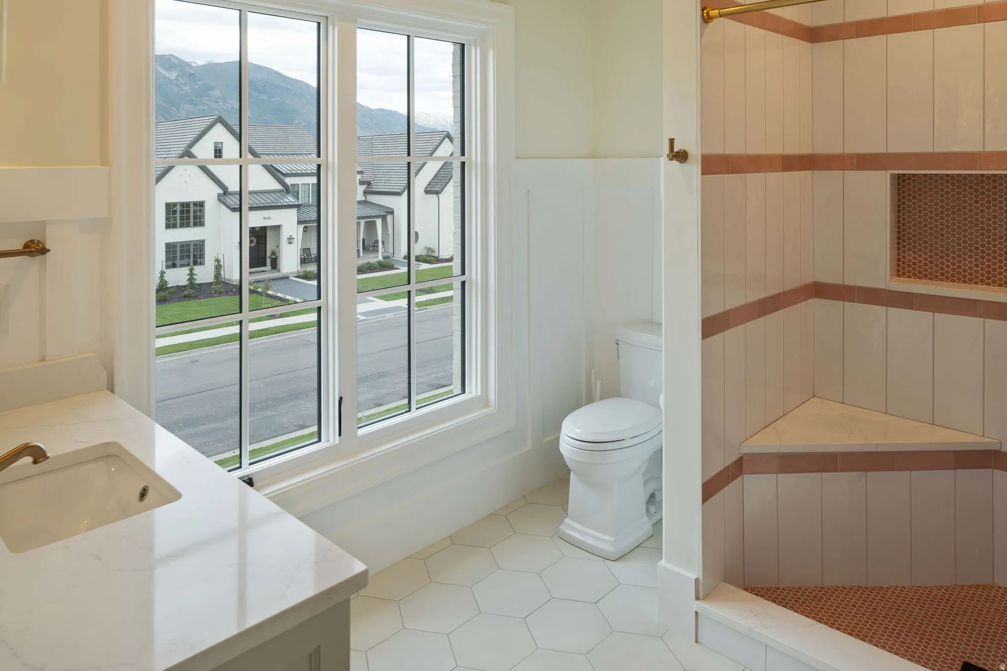 Bathroom featuring a white vanity with an undermount sink and light-toned countertop, a full-height window with grid panes, white hexagonal floor tiles, and a shower with light-toned vertical tiling and a built-in bench
