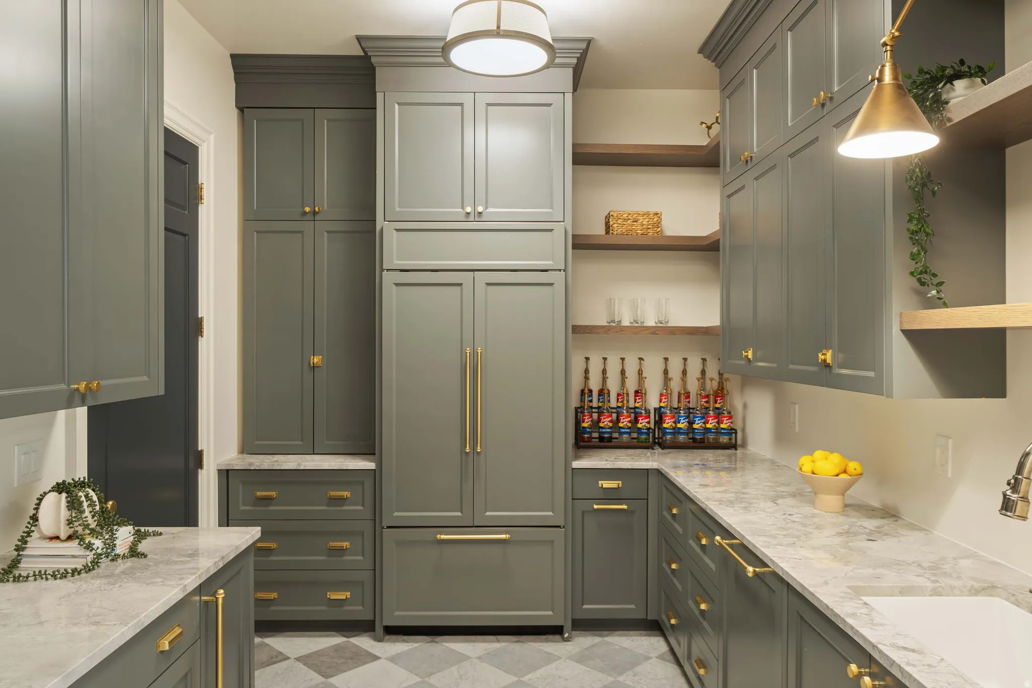 Spacious kitchen featuring extensive sage green cabinetry with gold-tone hardware, light-toned stone countertops, and a built-in paneled refrigerator