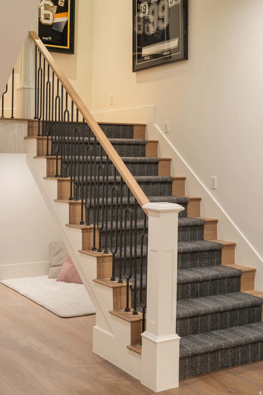 Staircase with wood-finish treads and a patterned carpet runner, featuring black wrought iron balusters and a natural wood handrail