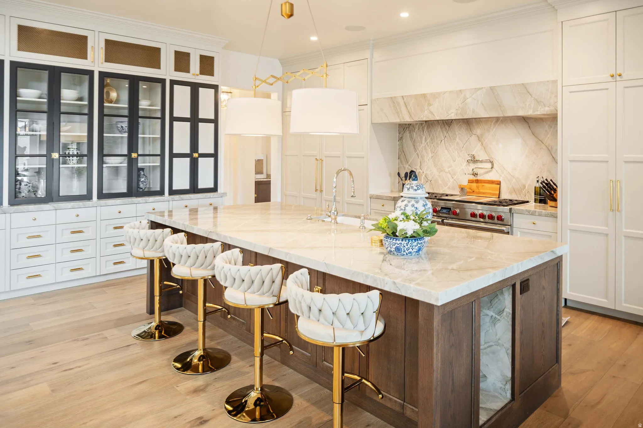 Spacious kitchen featuring a large central island with a built-in beverage cooler, light wood-finish flooring, a commercial-grade range with a stone slab backsplash, custom cabinetry, and glass-front upper cabinets