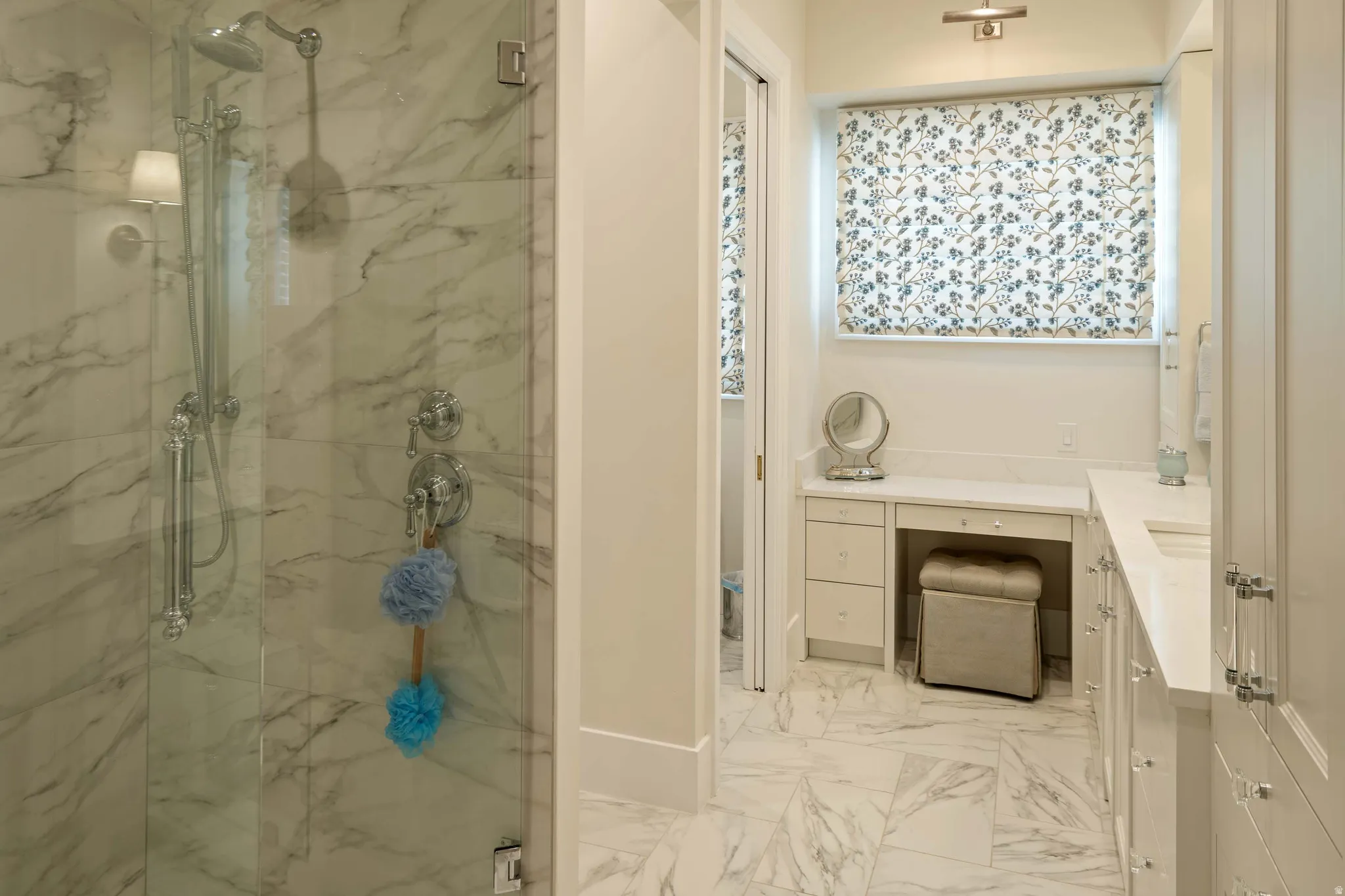 Spacious bathroom featuring a glass-enclosed shower with marble-finish tile, vanity countertop space, and built-in cabinetry with clear hardware