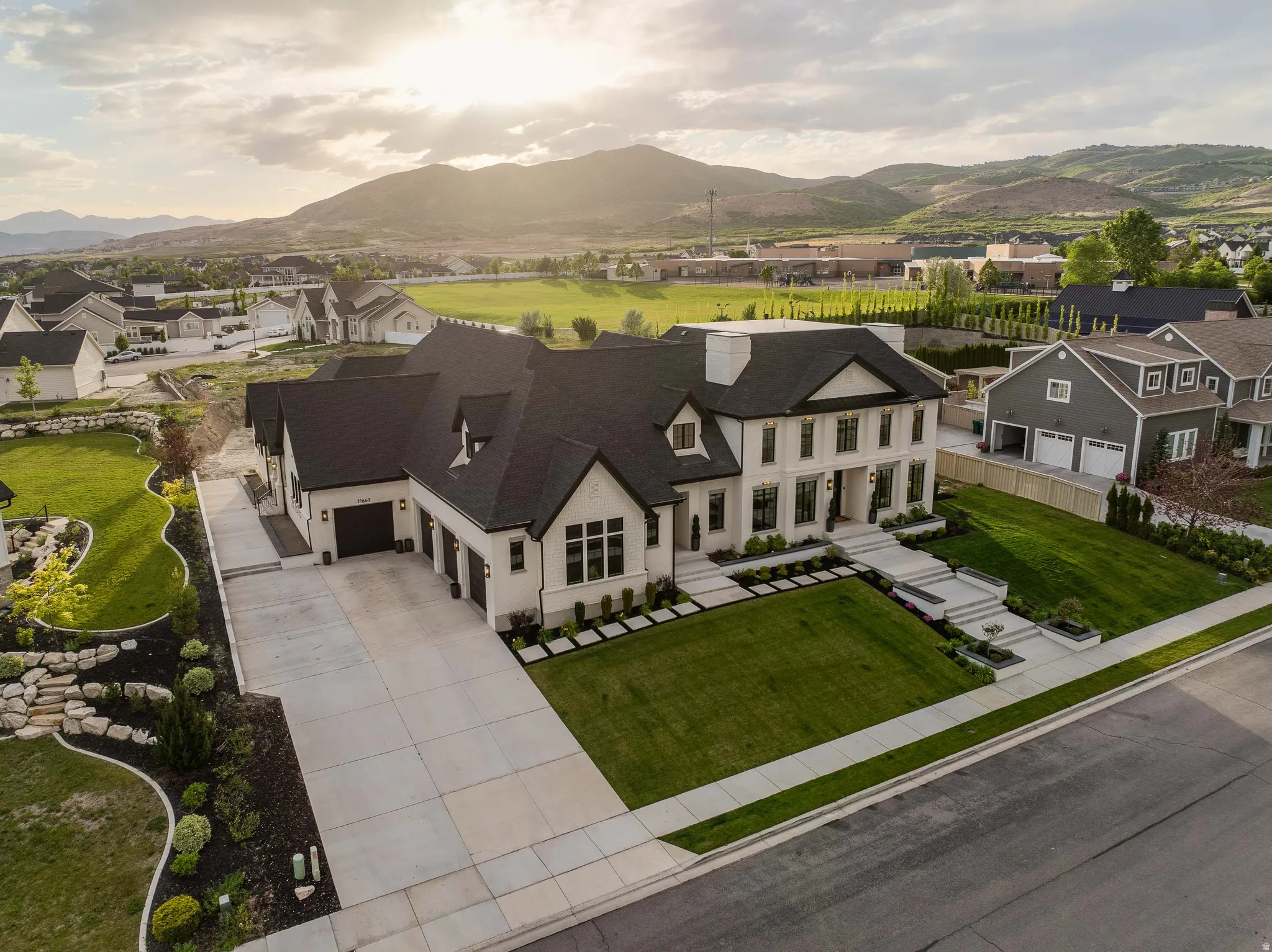 Contemporary residence featuring a light-colored stucco and stone exterior, a dark shingle roof, and multiple large windows