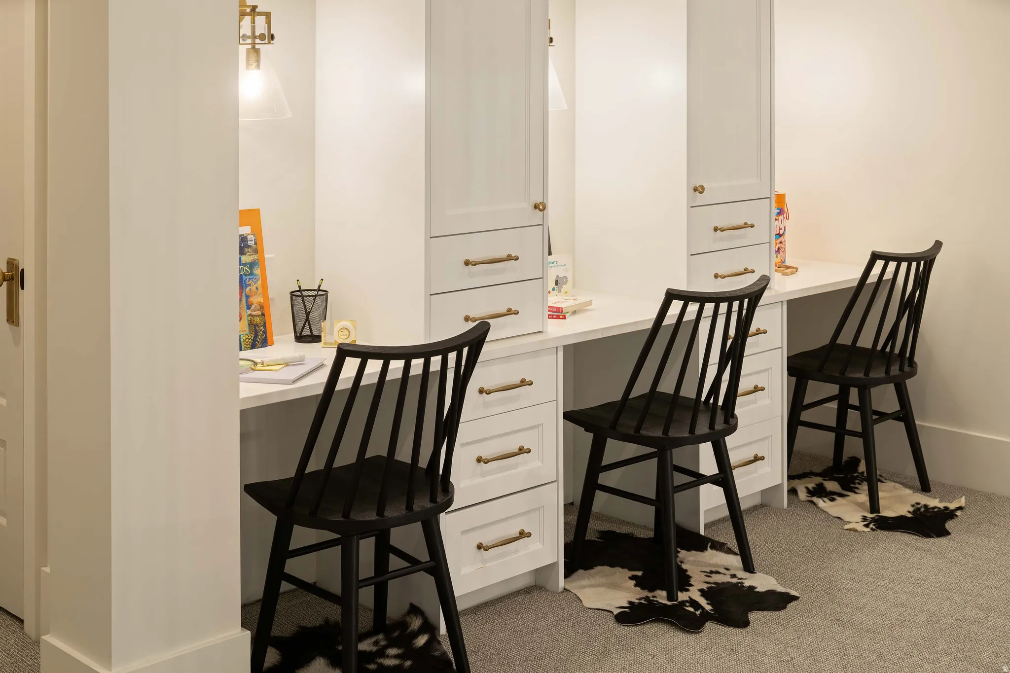 Built-in desk system featuring three workstations with white countertops, integrated cabinetry, and brass hardware