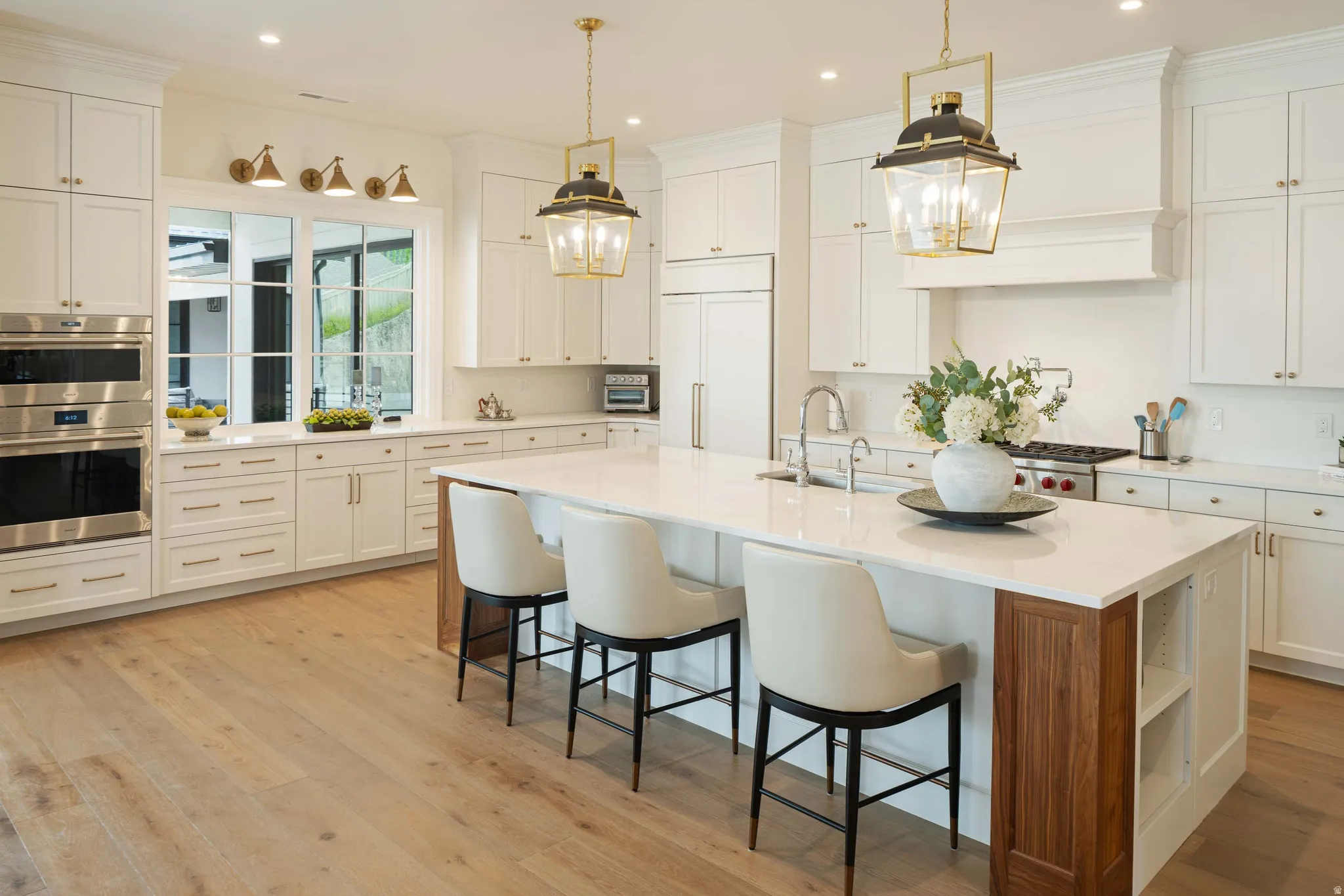 Gourmet kitchen featuring a large central island with light-toned countertop, extensive white cabinetry, stainless steel double ovens, and wood-finish flooring