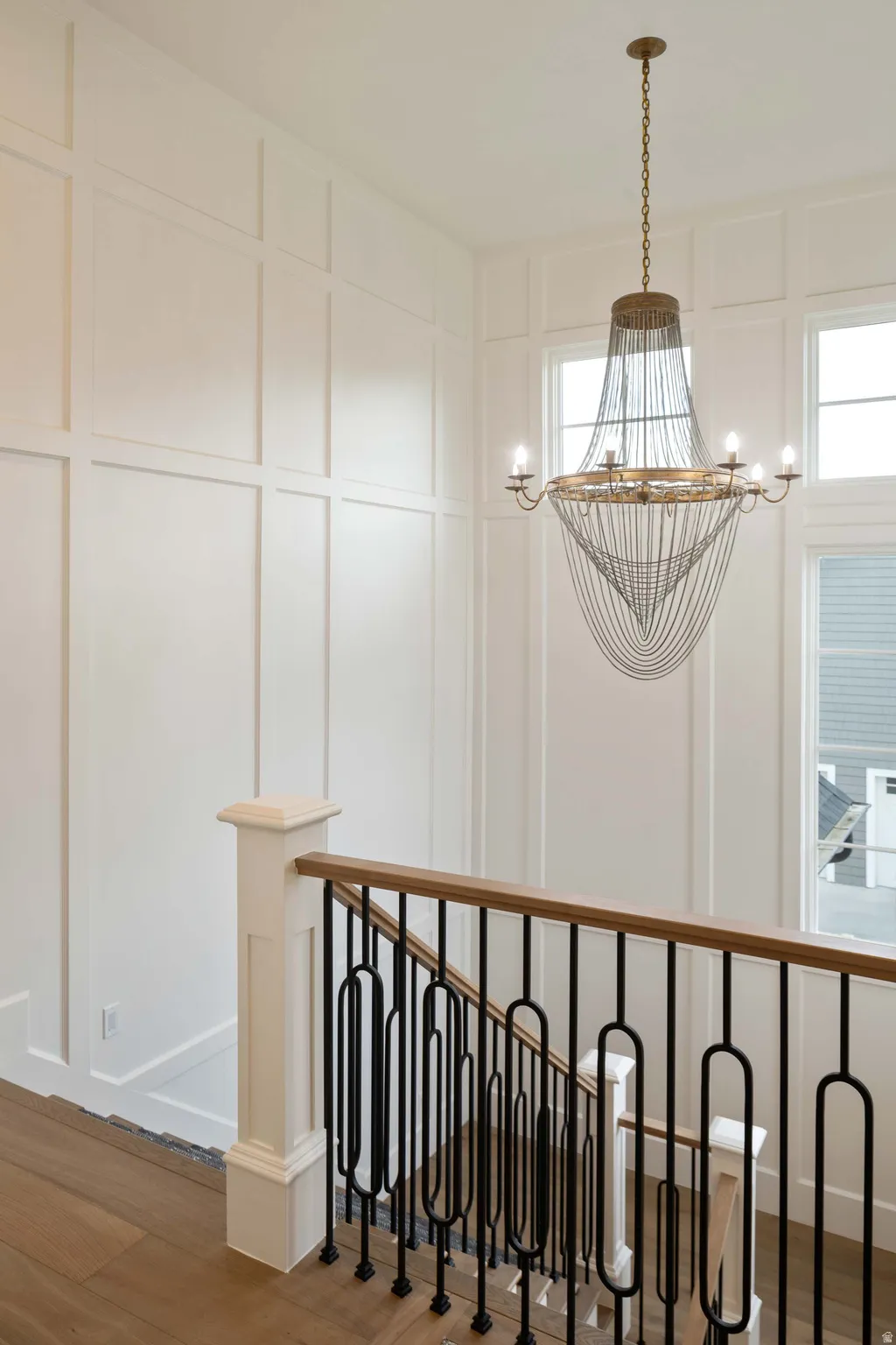 Staircase featuring wood-finish flooring, custom iron balusters, a wood handrail, and wainscoting