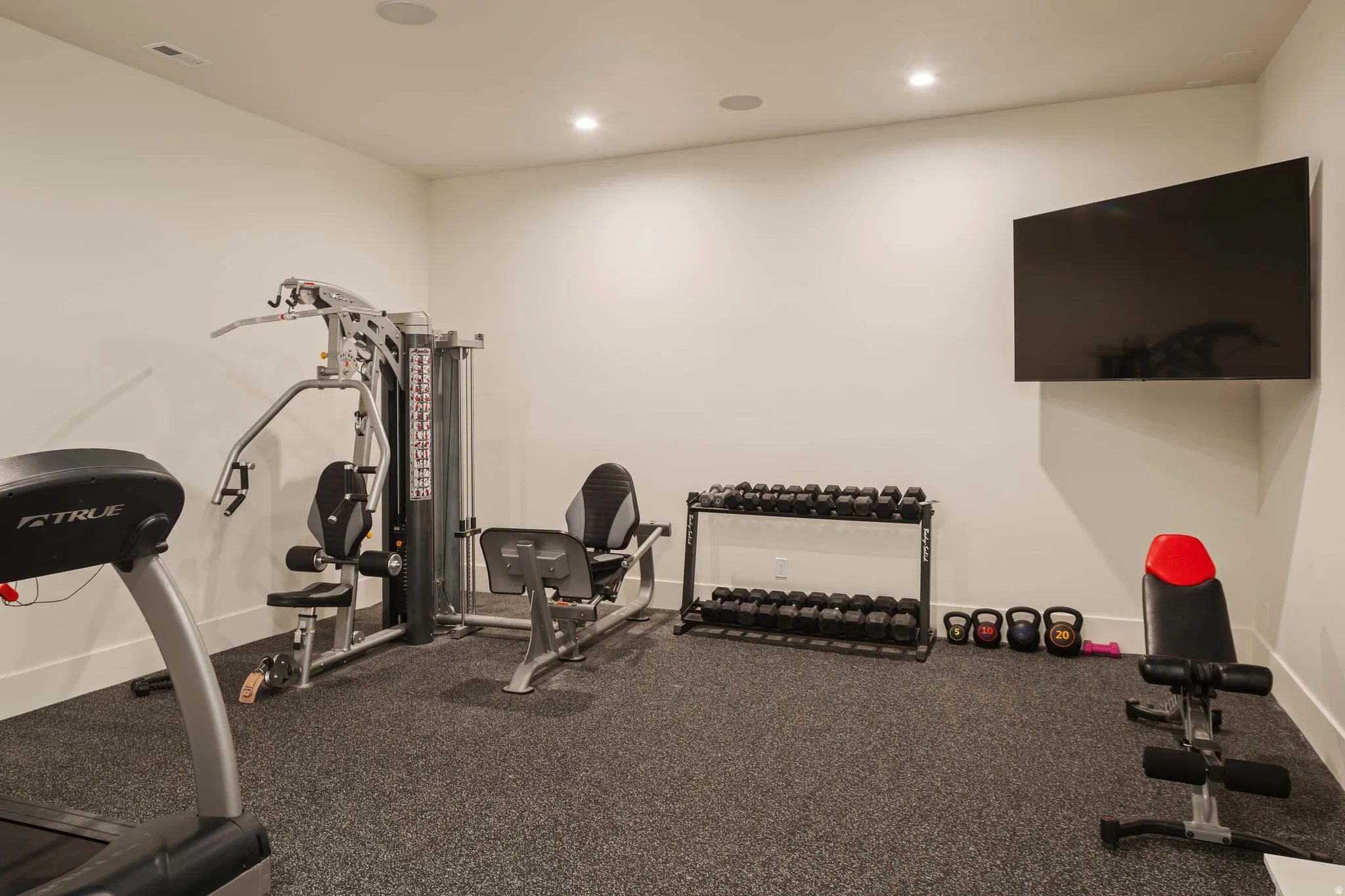 Dedicated exercise room featuring a wall-mounted television, recessed lighting, and resilient rubber flooring