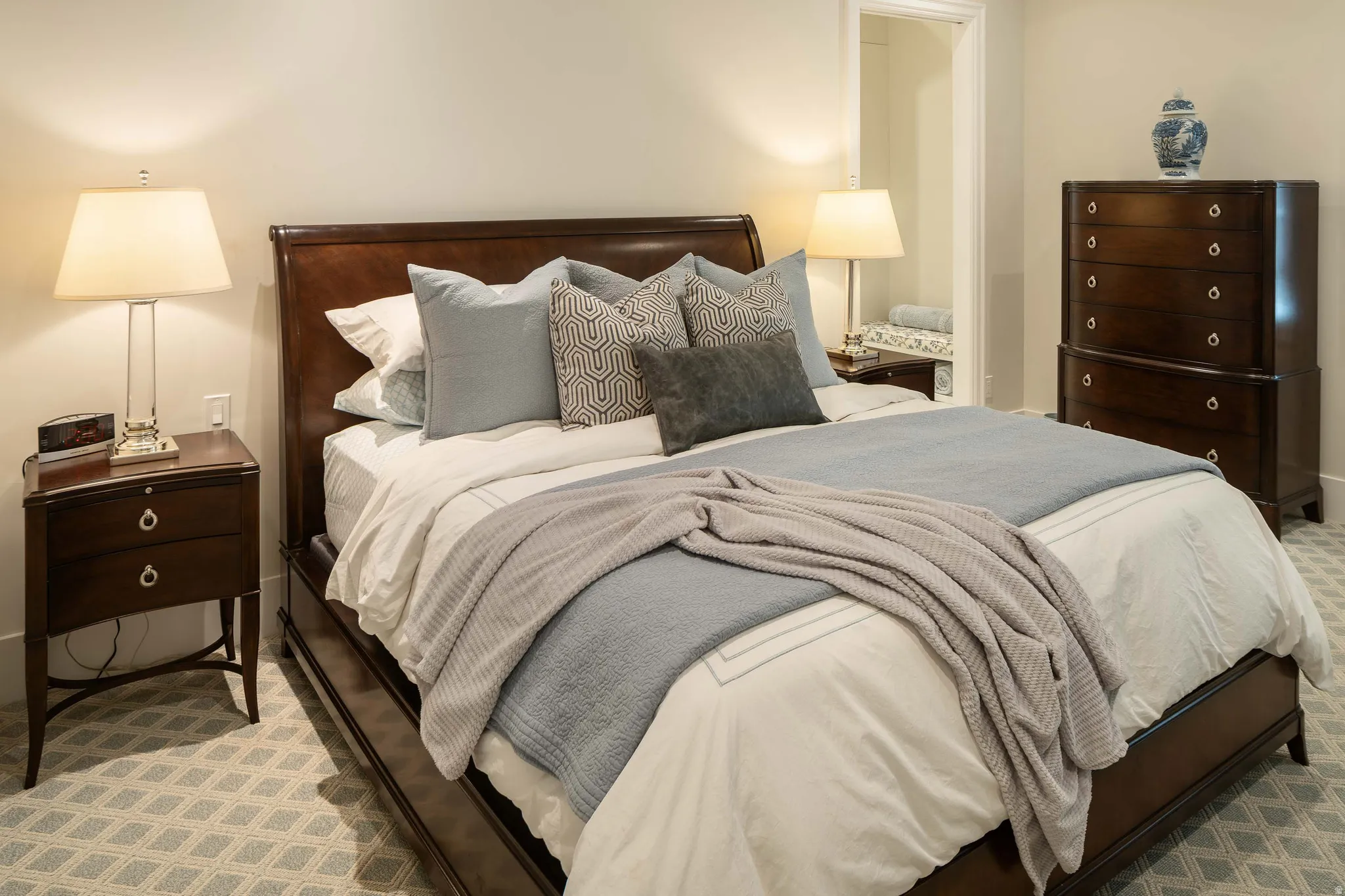 Carpeted bedroom featuring a dark wood bed frame, two built-in nightstands with ring pull hardware, and a tall chest of drawers
