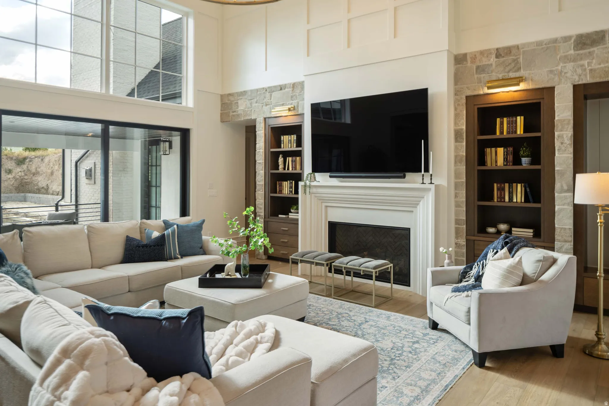 Living area featuring a stone accent wall, fireplace with a decorative mantel, built-in shelving, two-story windows, and wood-finish flooring