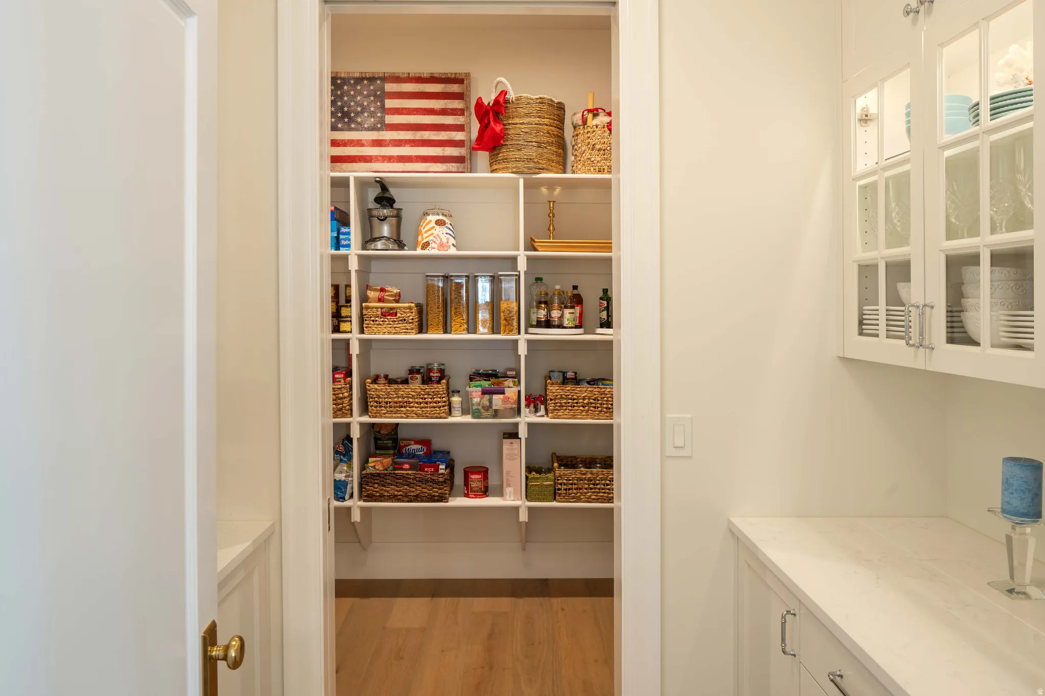 Bright white pantry with extensive shelving, wood-finish flooring, and a solid-surface countertop with white cabinetry