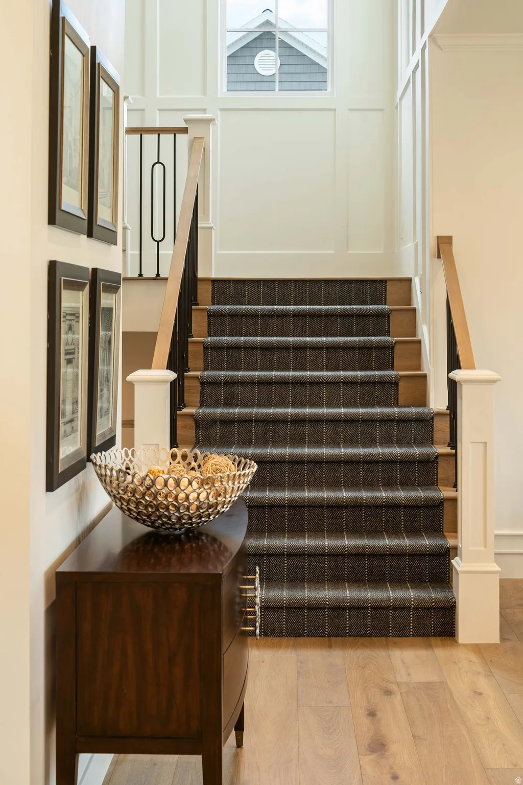 Staircase featuring wood treads with a plaid carpet runner, light wood-finish flooring, and white board and batten wall paneling