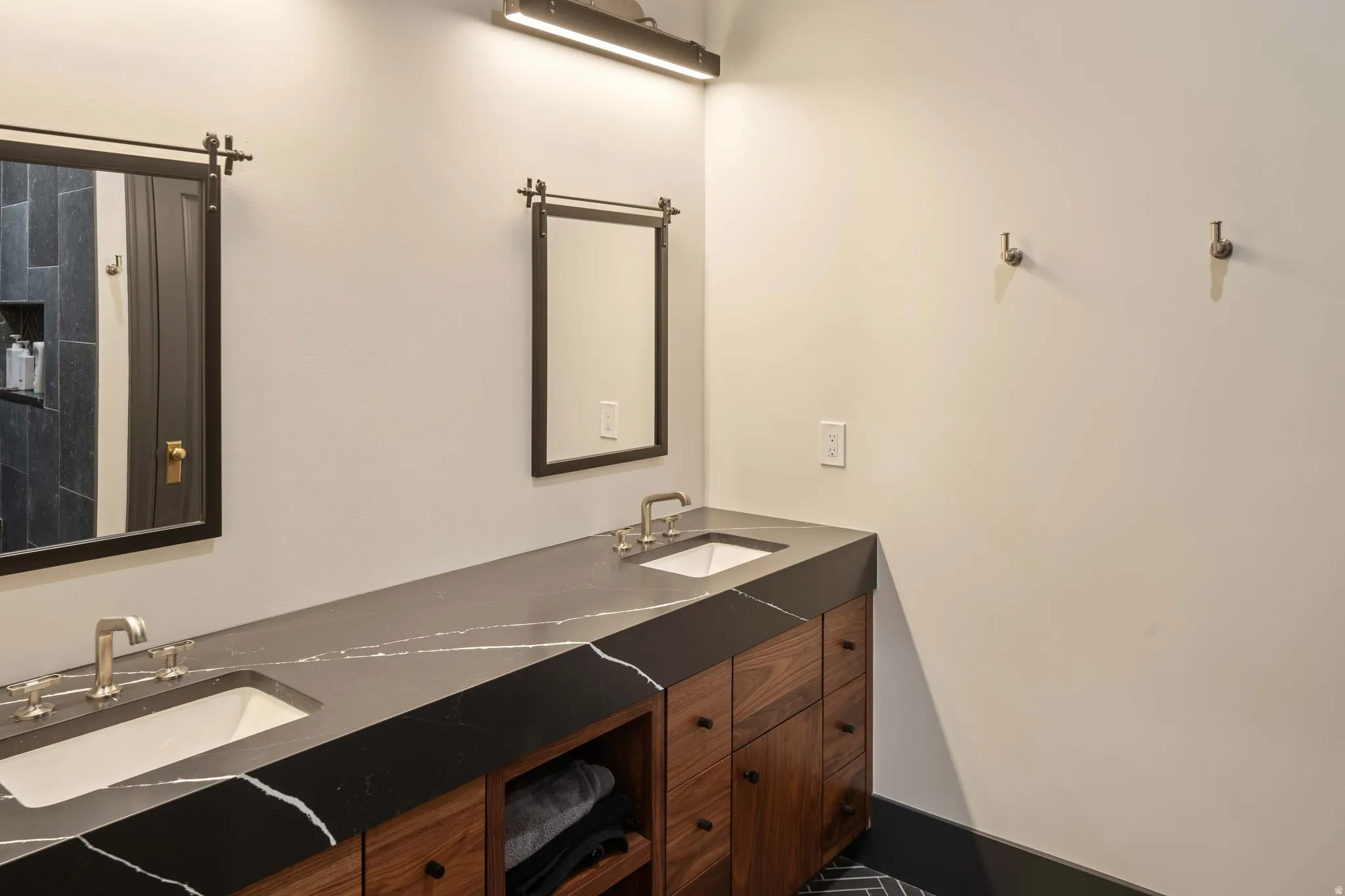 Dual vanity featuring rich wood-finish cabinetry and a dark countertop with pronounced white veining