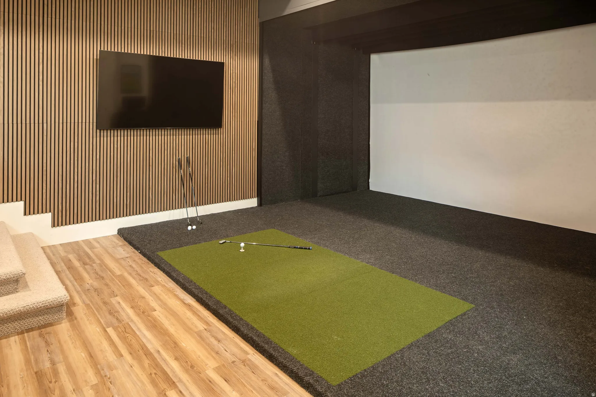 Dedicated golf simulator space featuring a large projection screen, padded flooring, and a green putting mat