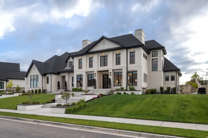 Stately multi-story residence featuring light-colored brick and dark roofing, multiple gables, a prominent front entrance with transom windows, and extensive landscaping with tiered planters