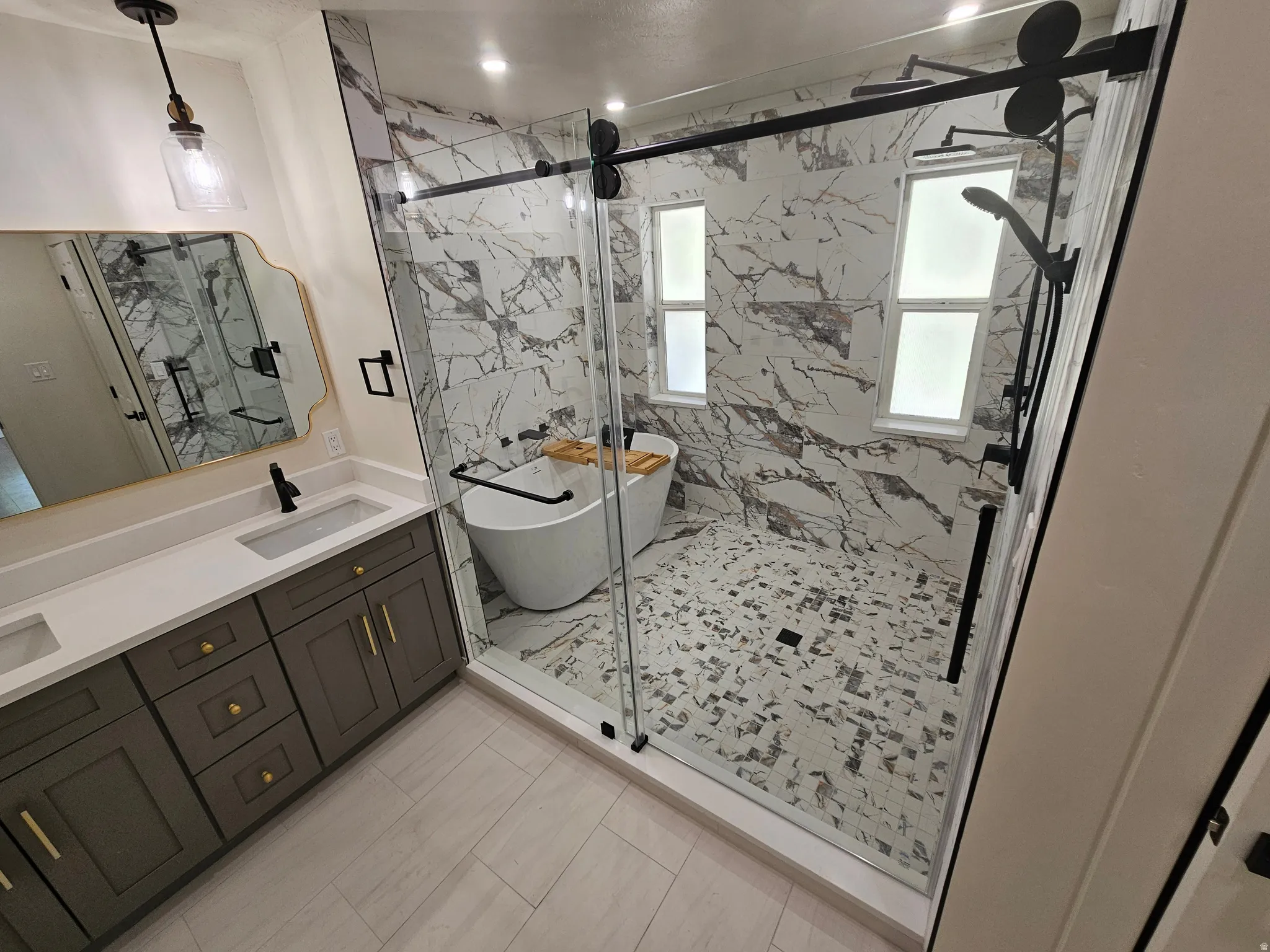 Bathroom featuring a dual vanity with a light-toned countertop, a frameless glass shower enclosure, a freestanding soaking tub, and a multi-function shower system