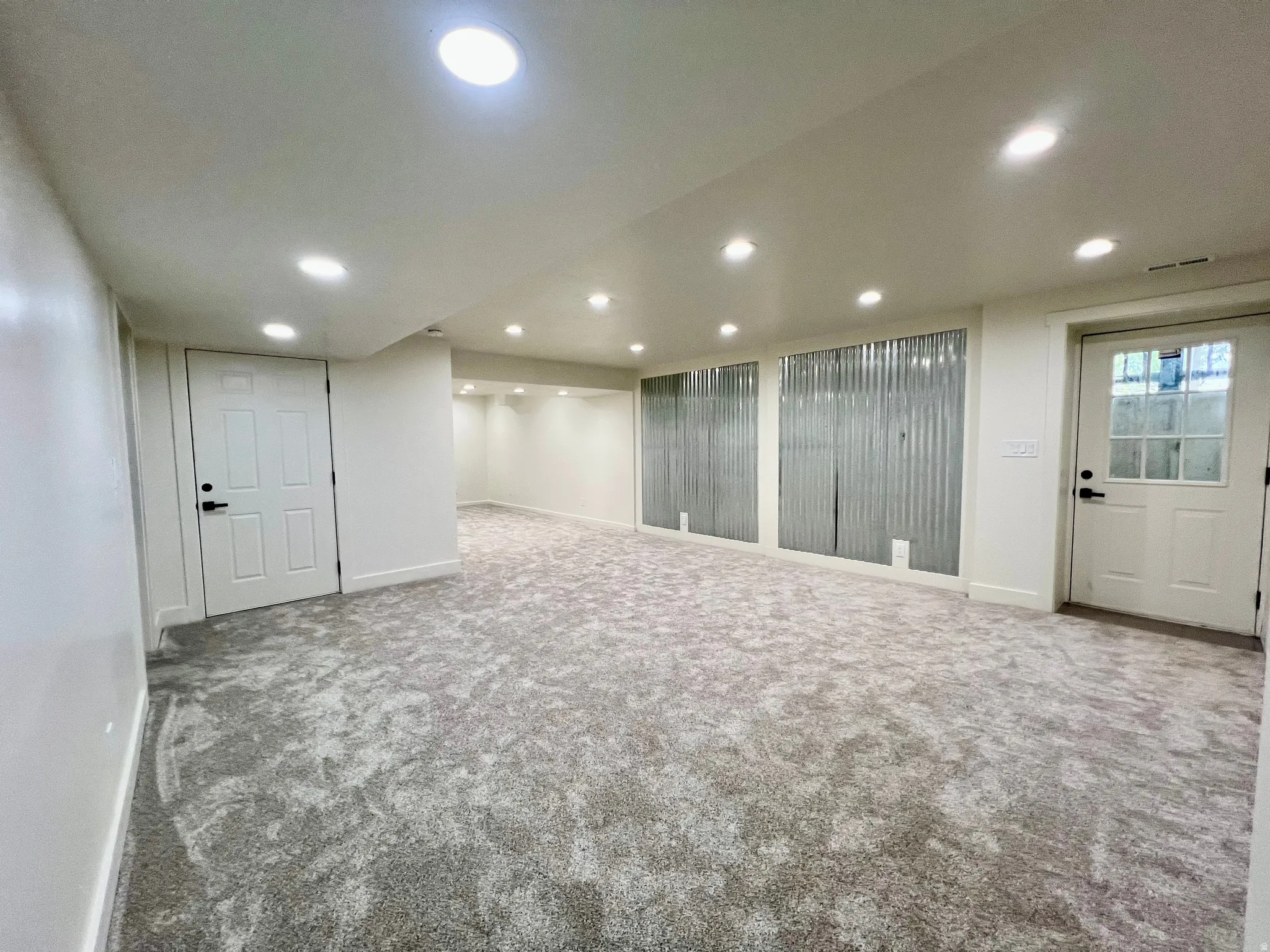 Spacious finished room featuring recessed lighting, light-toned textured carpet, white panel doors, and corrugated metal wall accents