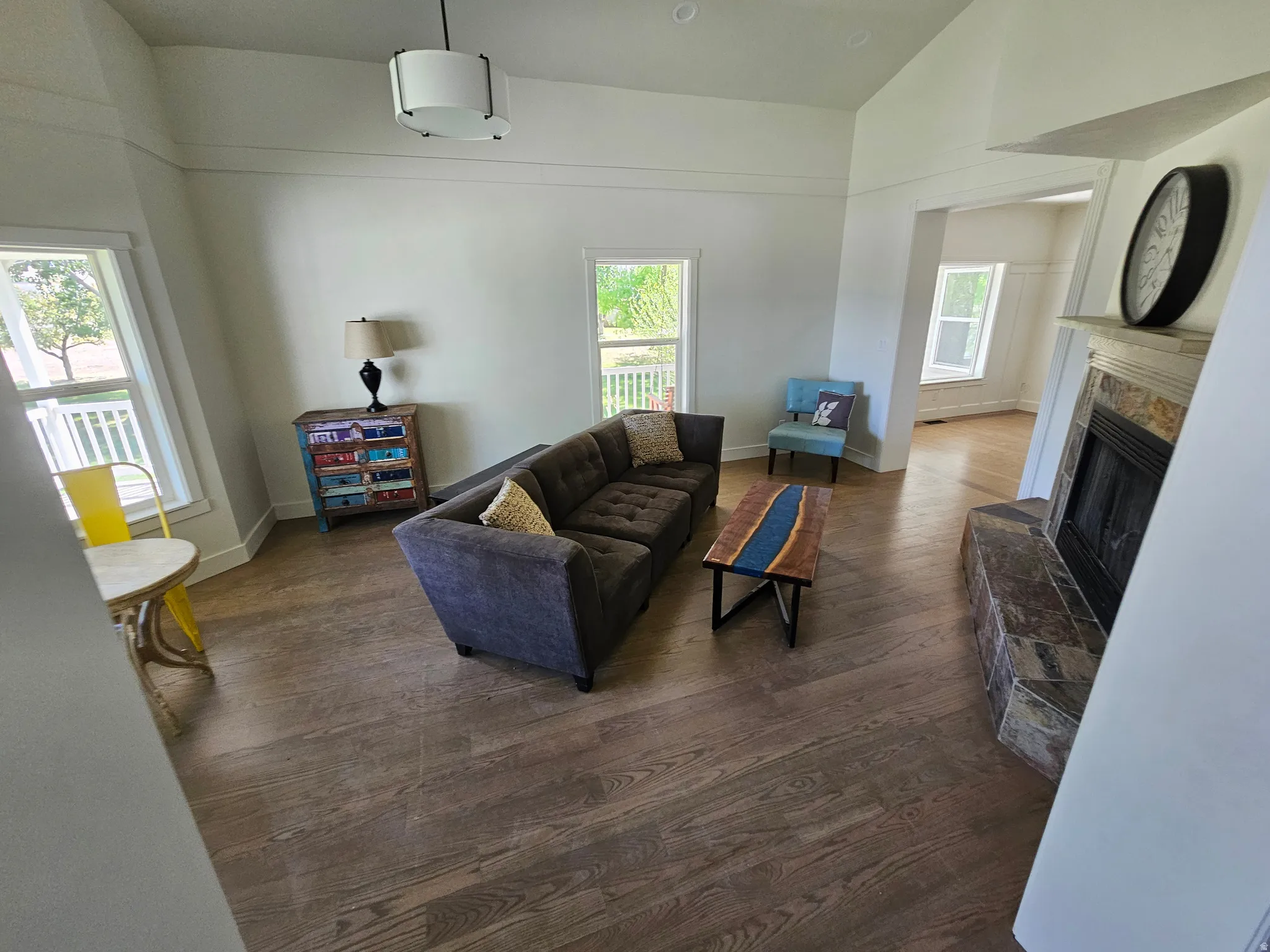 Spacious living area featuring wood-finish flooring, a corner fireplace with stone surround, and abundant natural light from multiple windows